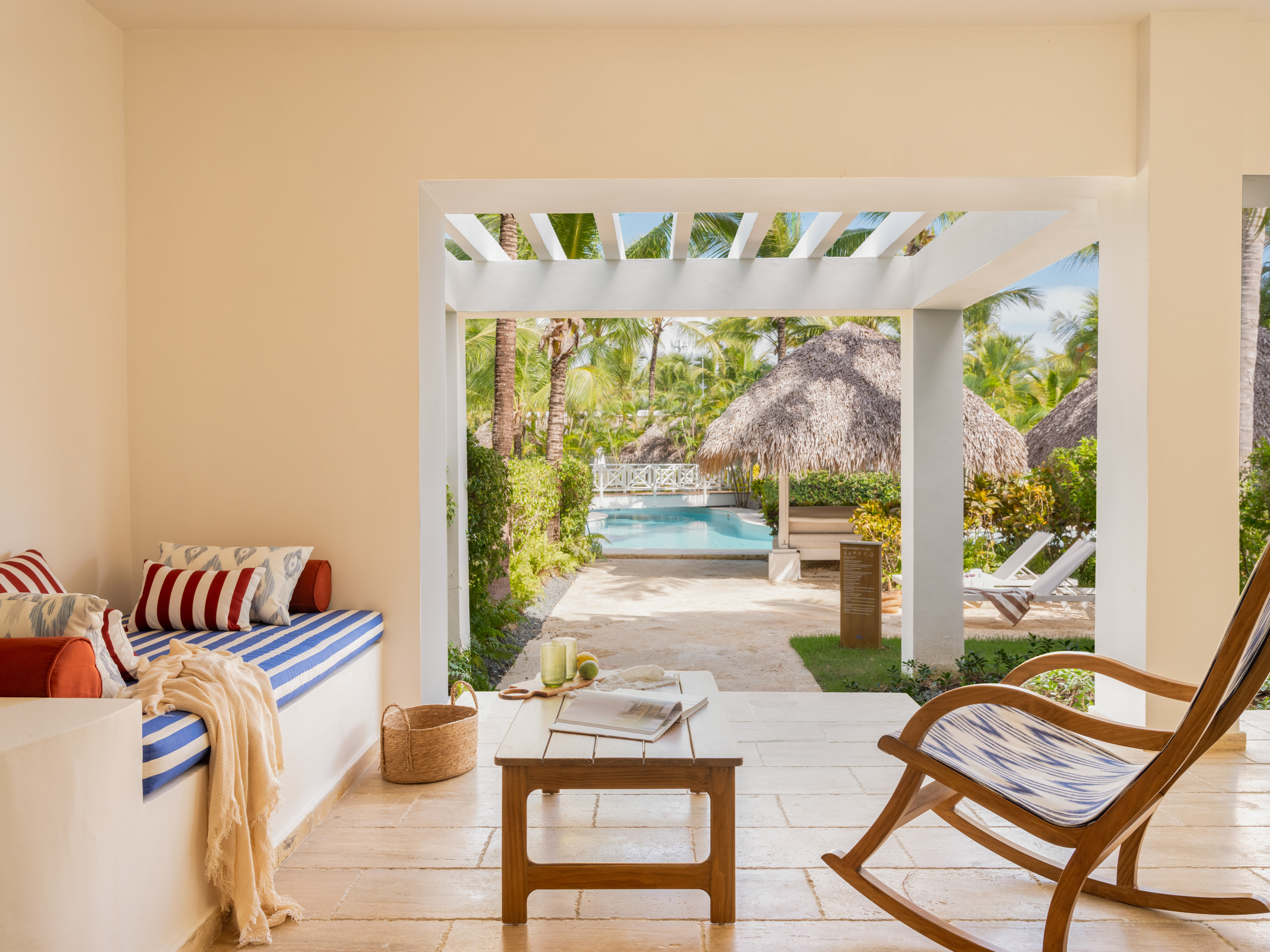 Tropical patio with pool view, rocking chair, palm trees, and striped bench.