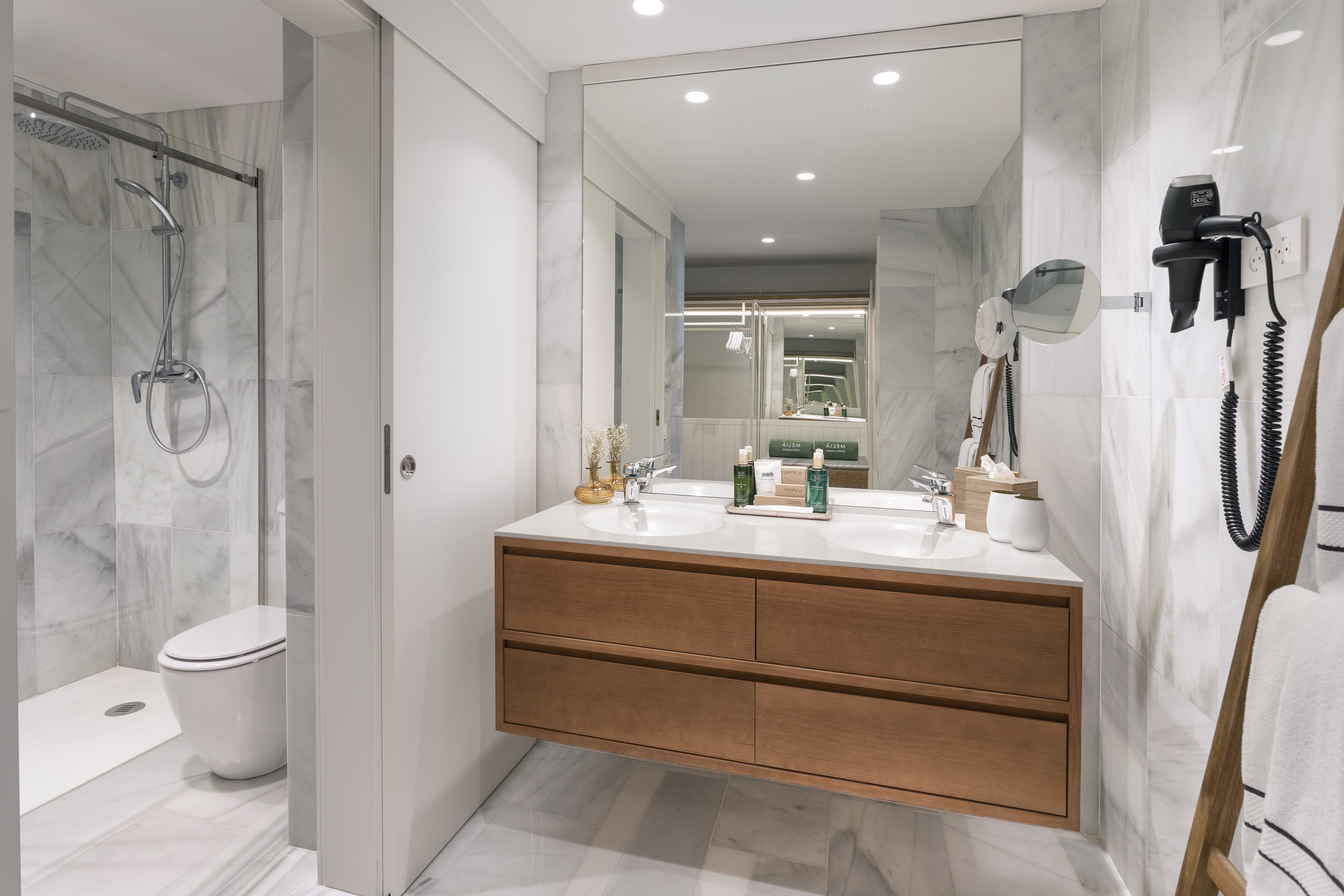 Modern hotel bathroom with white marble, double vanity, shower, and toilet.