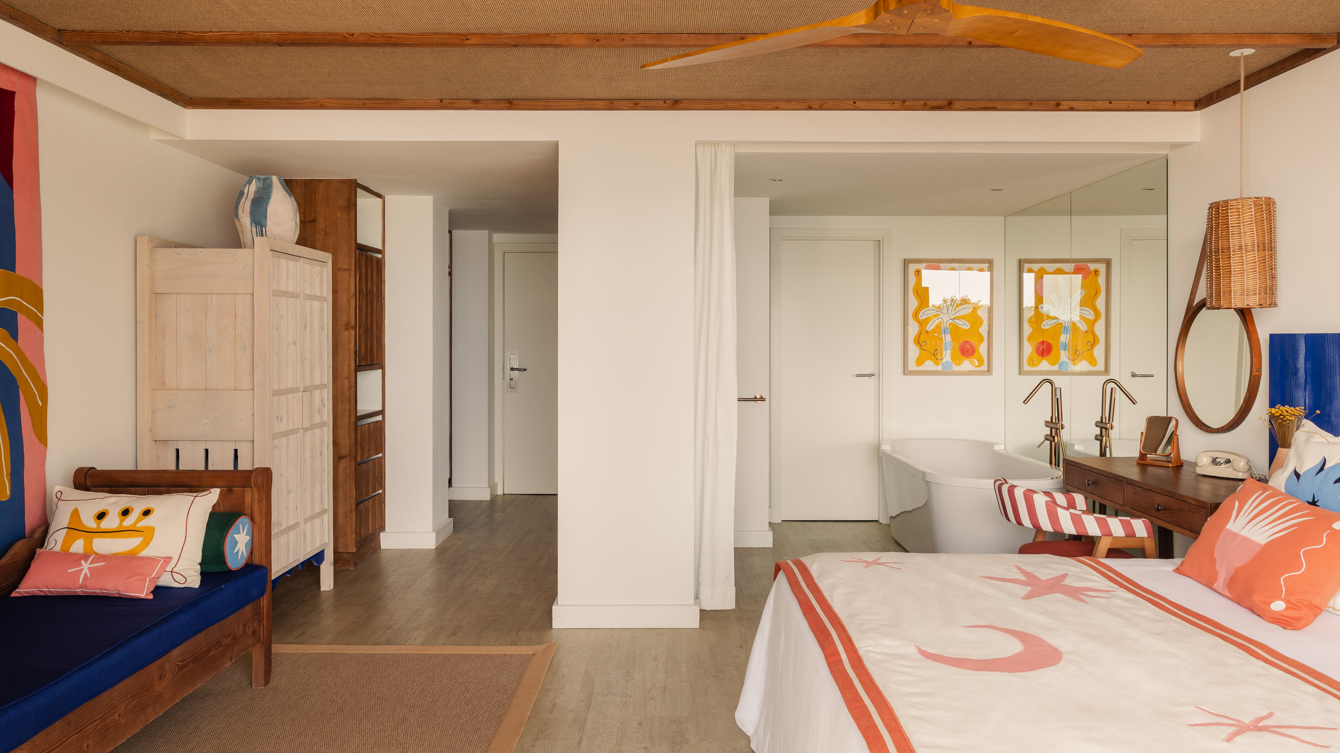 Vibrant hotel suite: patterned bed, daybed, wooden furniture, freestanding tub.