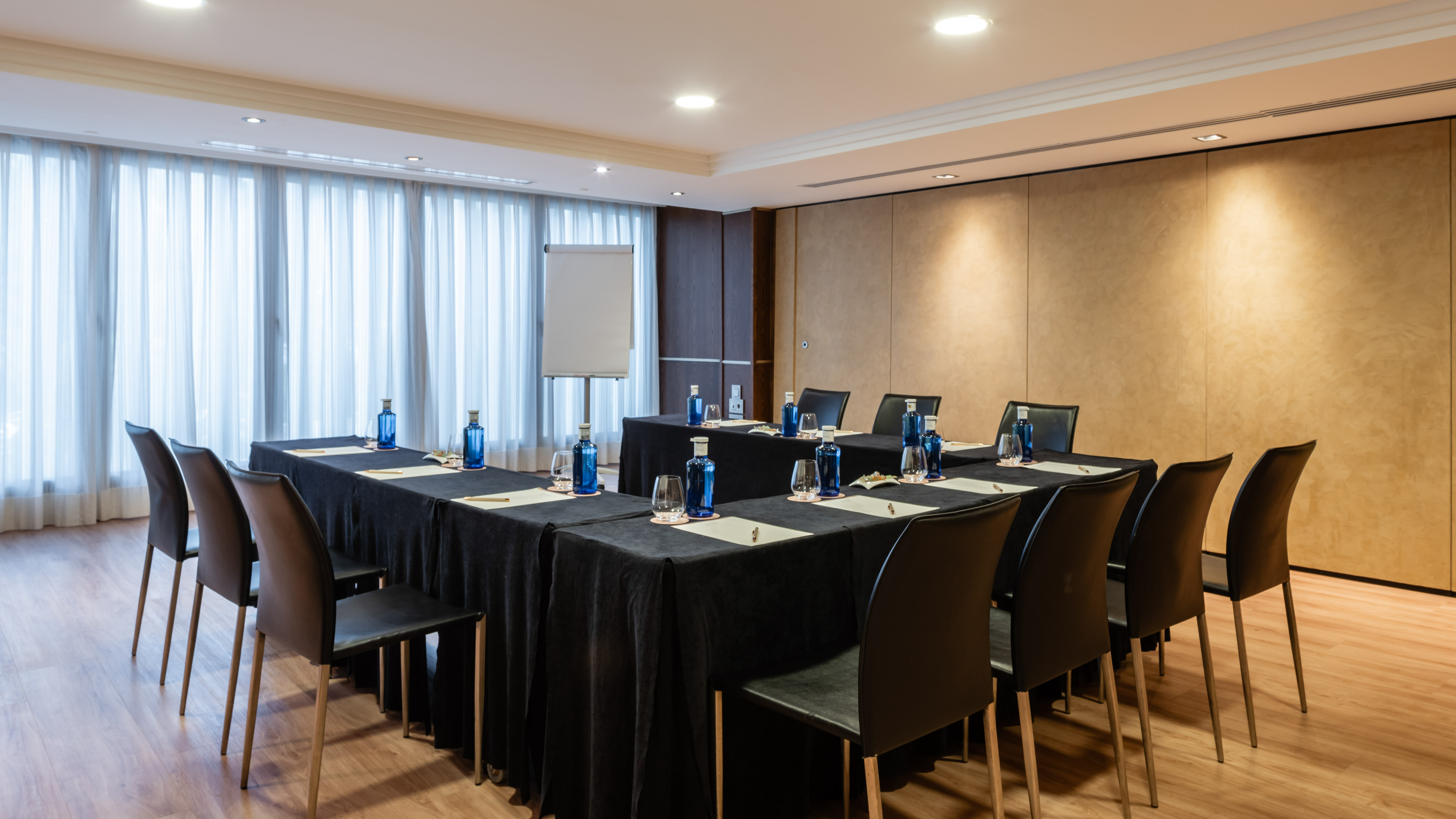 U-shaped conference room setup with black chairs, water bottles, and flipchart.