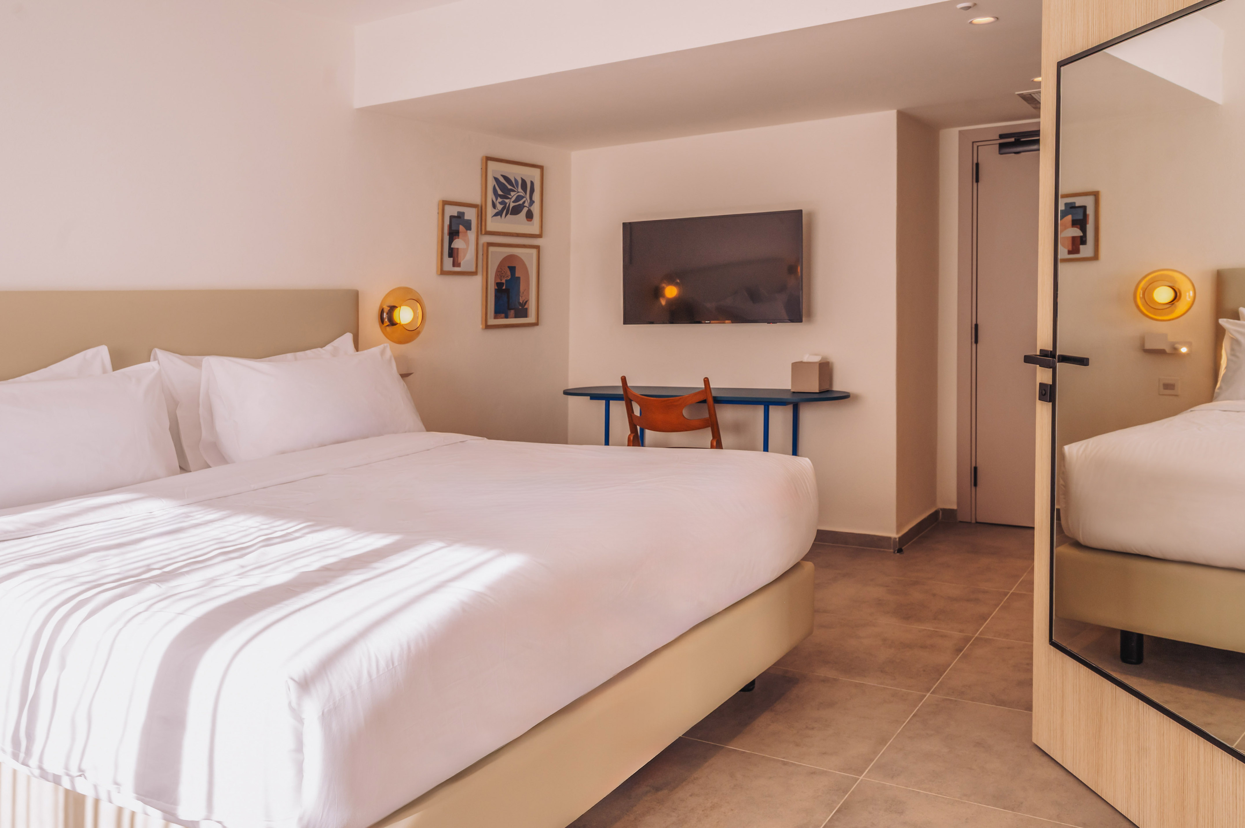 Modern hotel room with large bed, wall TV, desk, and contemporary art prints.