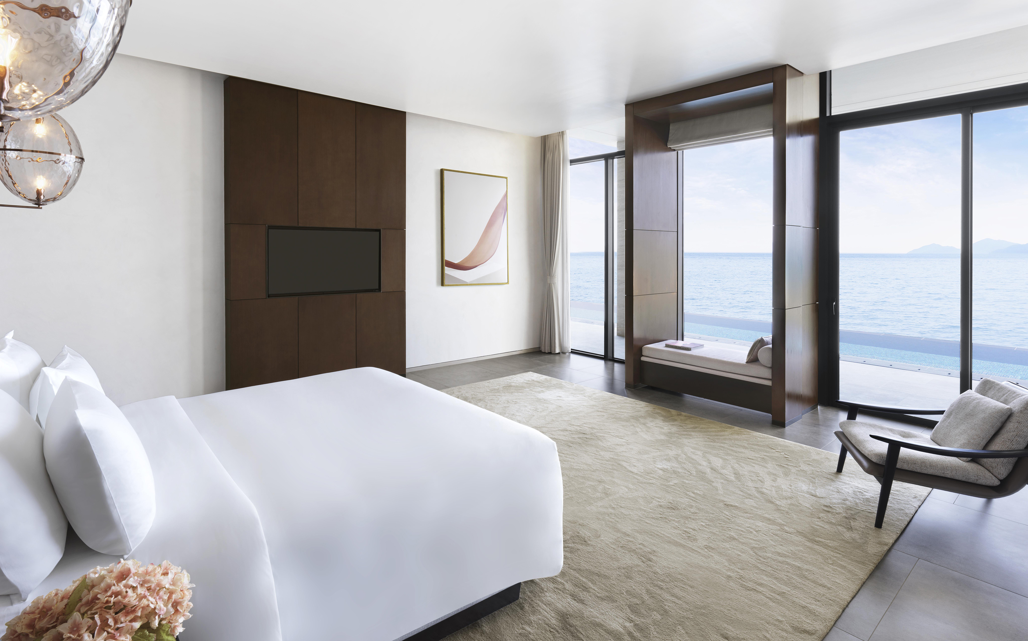 Luxury ocean view bedroom with white bed, large windows, and modern TV.