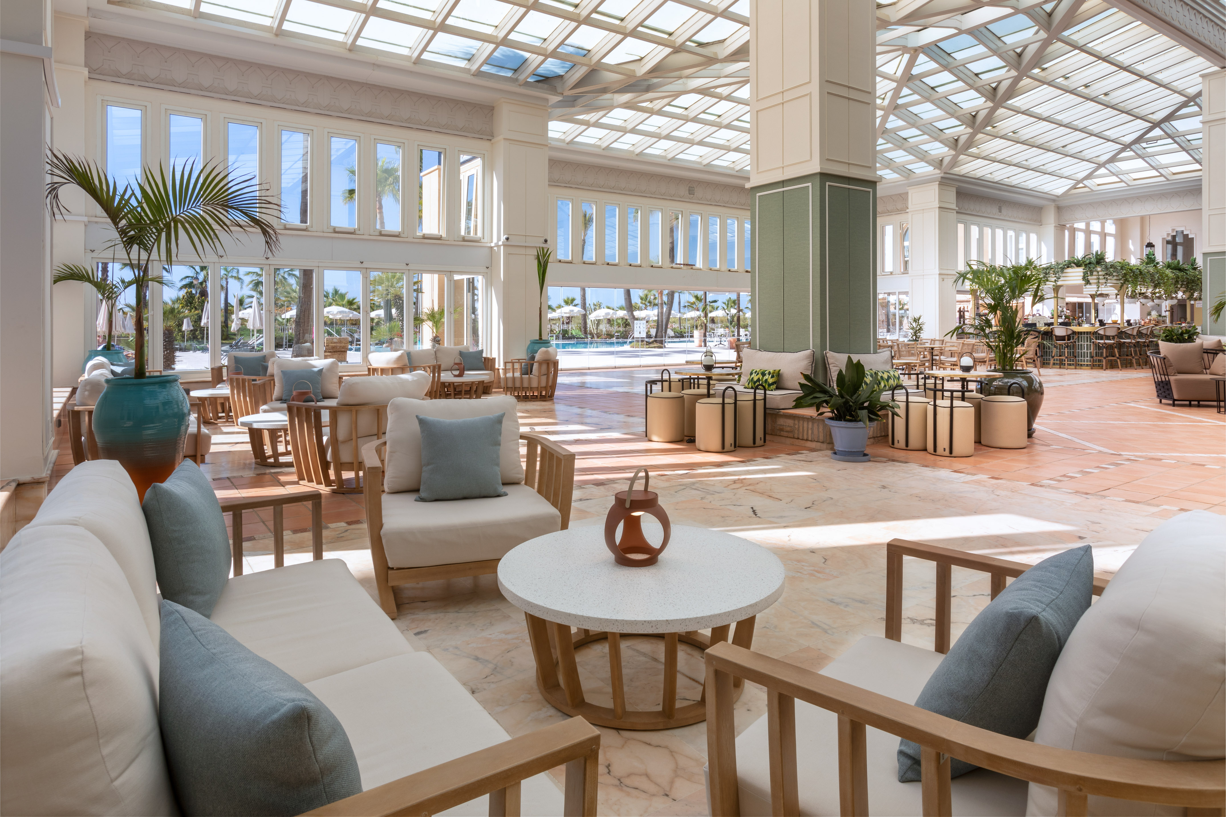Sunny resort lounge with glass roof, comfortable seating, and pool view.