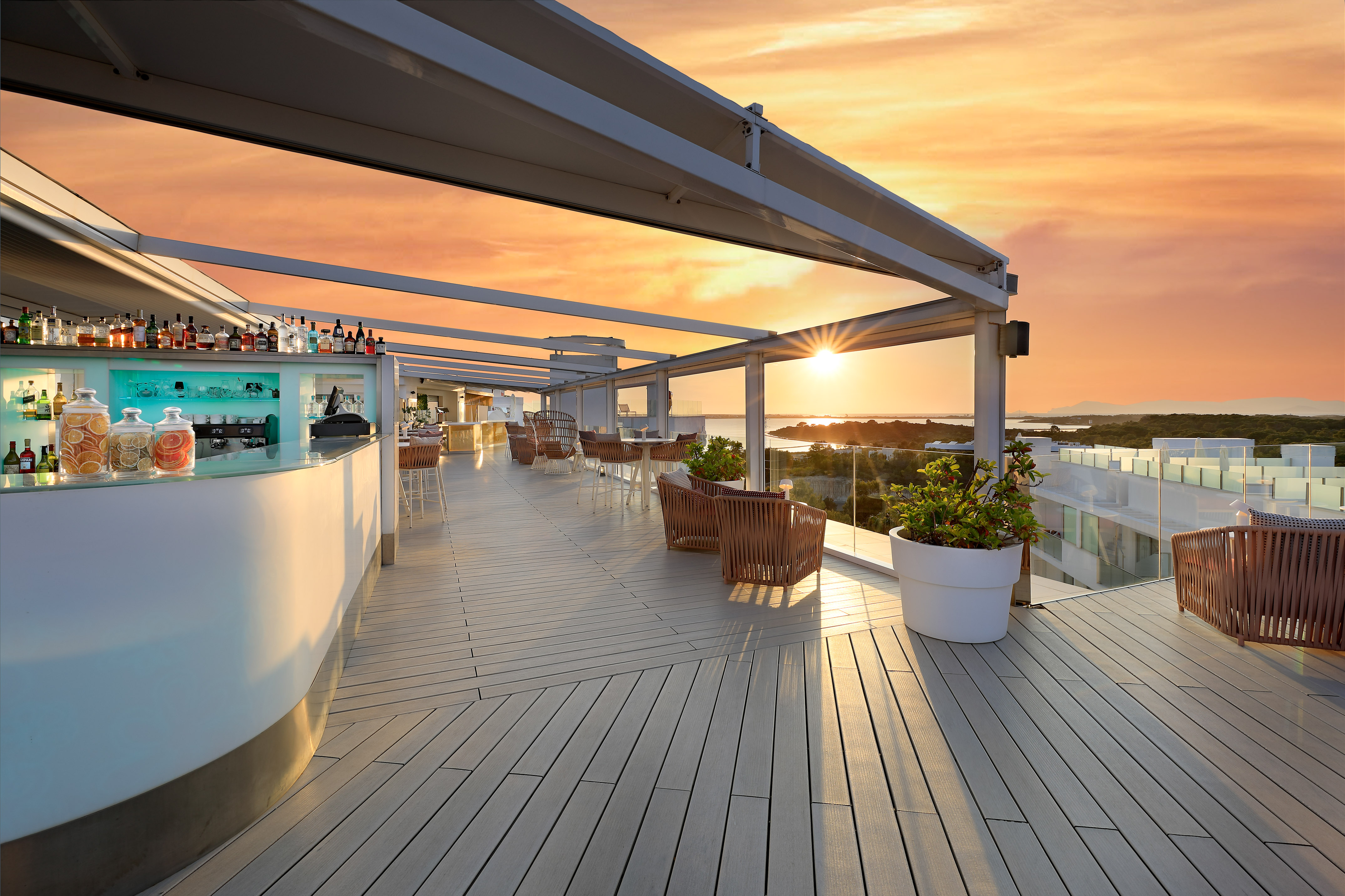 Rooftop bar with sunset ocean view, modern outdoor lounge and wooden deck.