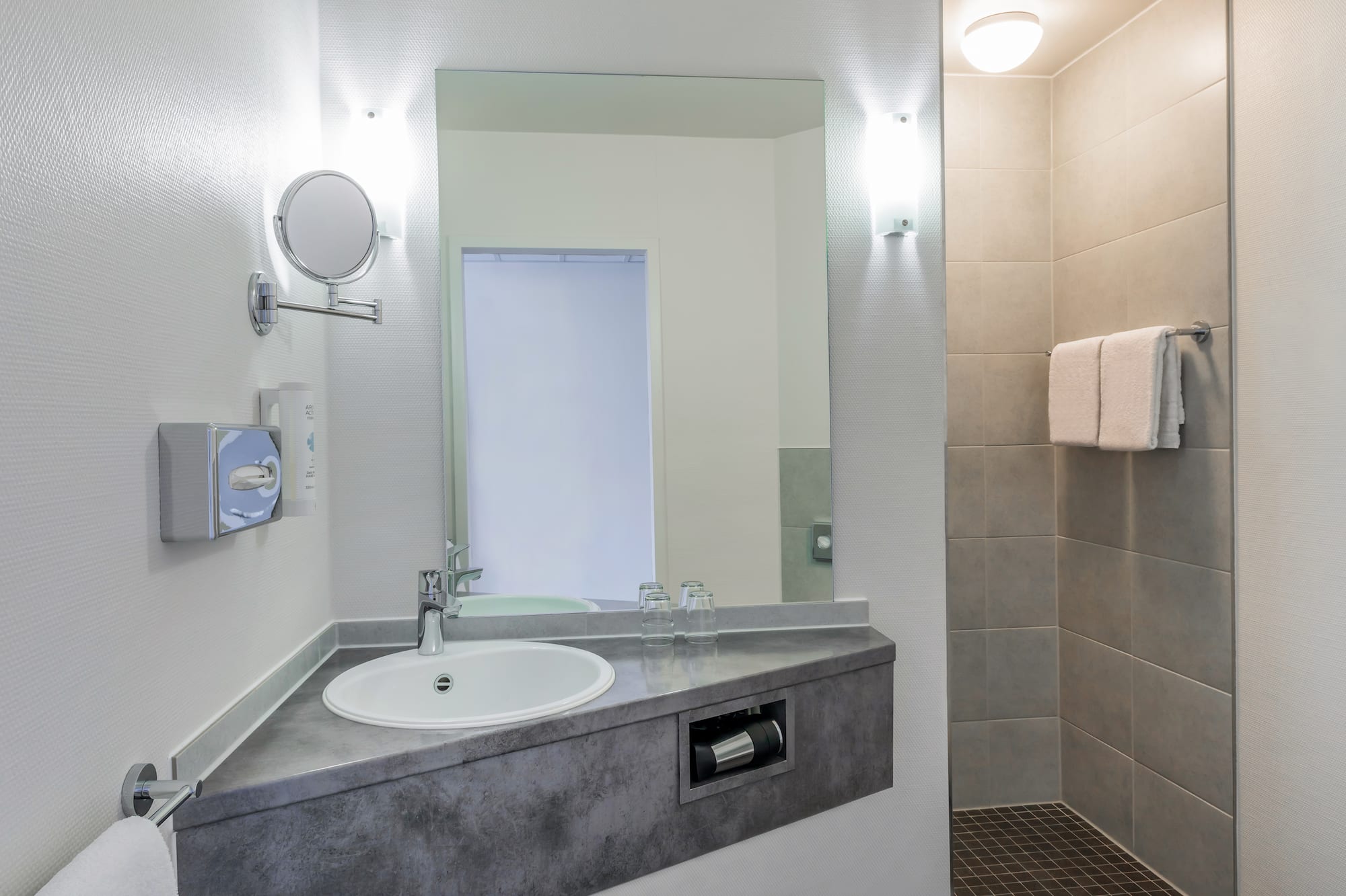 Modern bathroom with white sink, mirror, magnifying mirror, and tiled shower.
