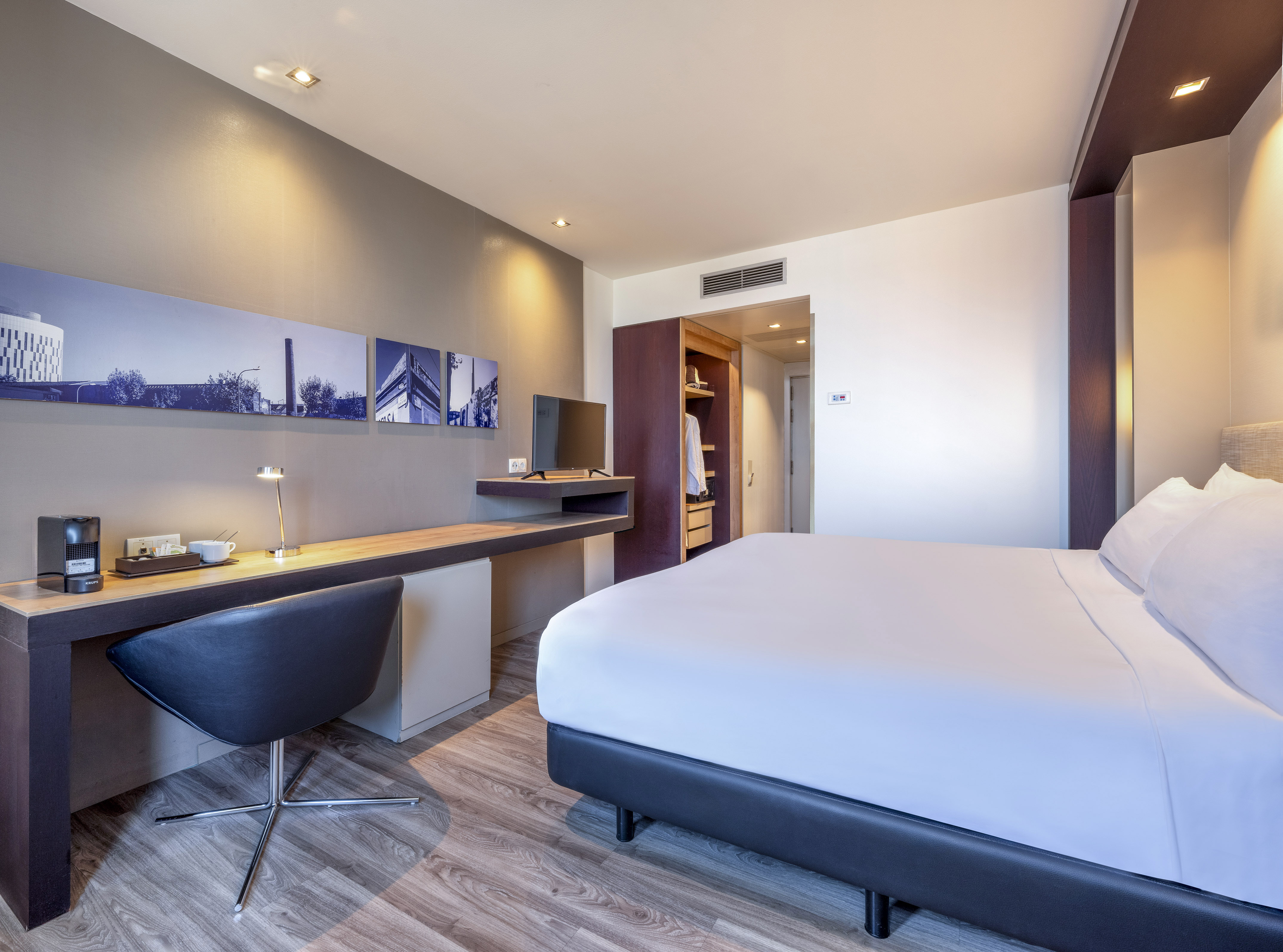 Stylish hotel bedroom with king bed, desk, coffee machine, and cityscape wall art.
