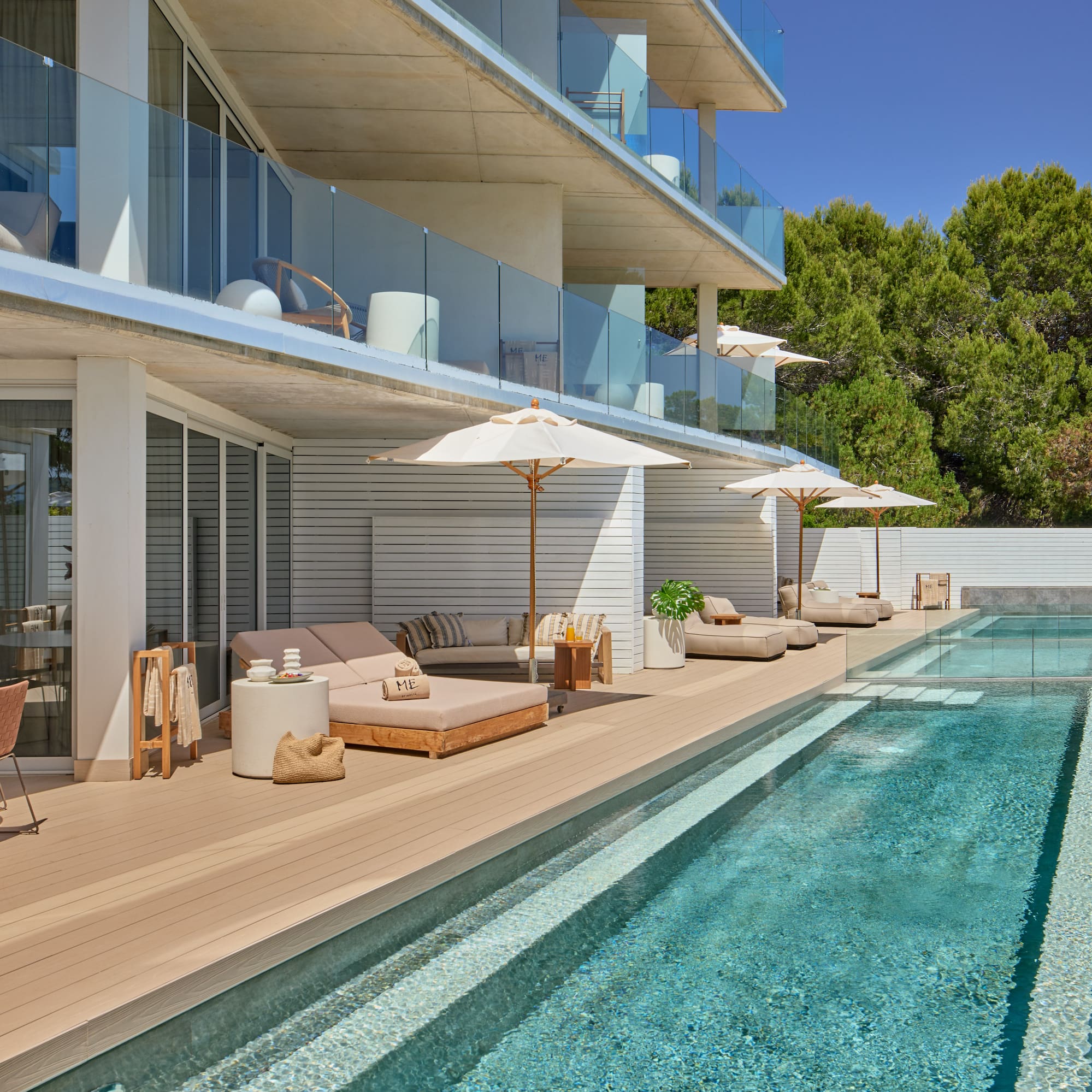 Modern hotel pool deck with sun loungers, private balconies, and lush trees.