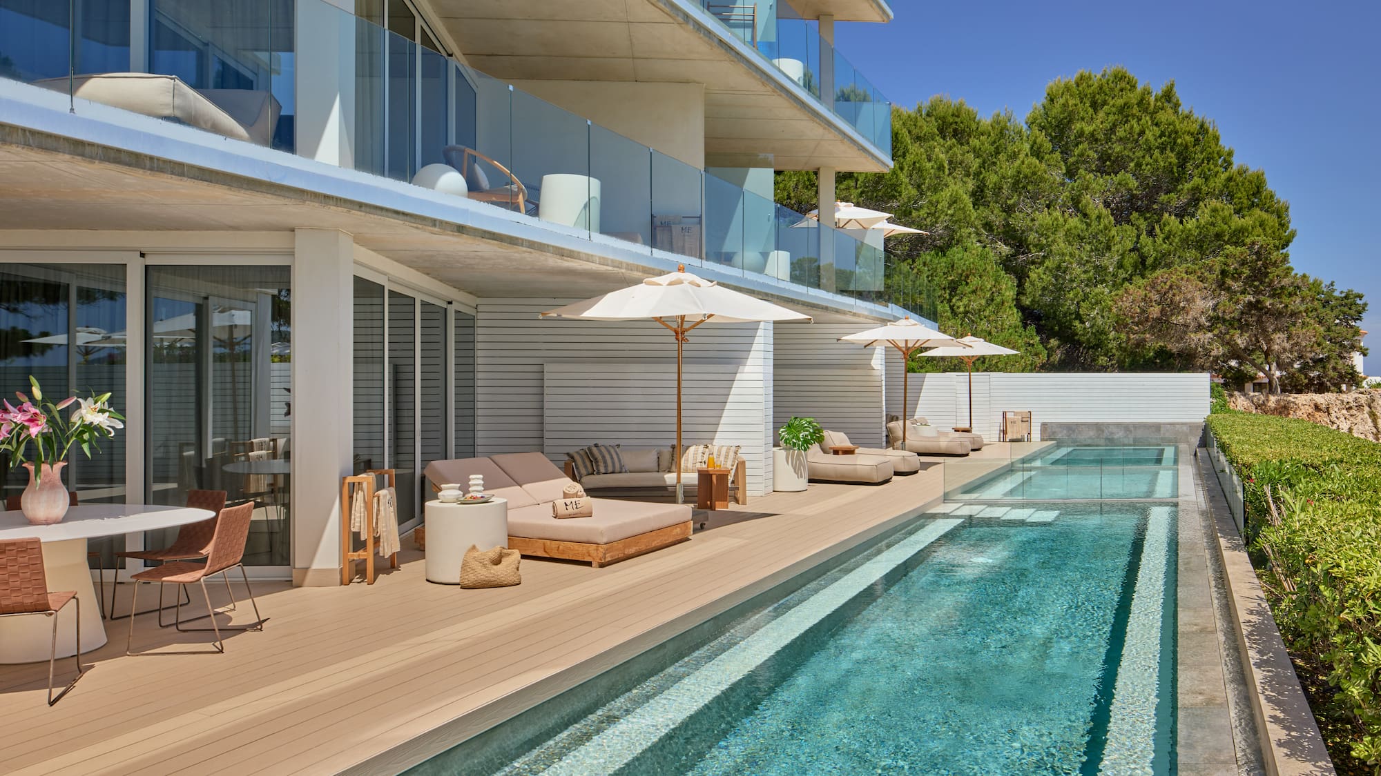 Modern hotel pool deck with sun loungers, private balconies, and lush trees.