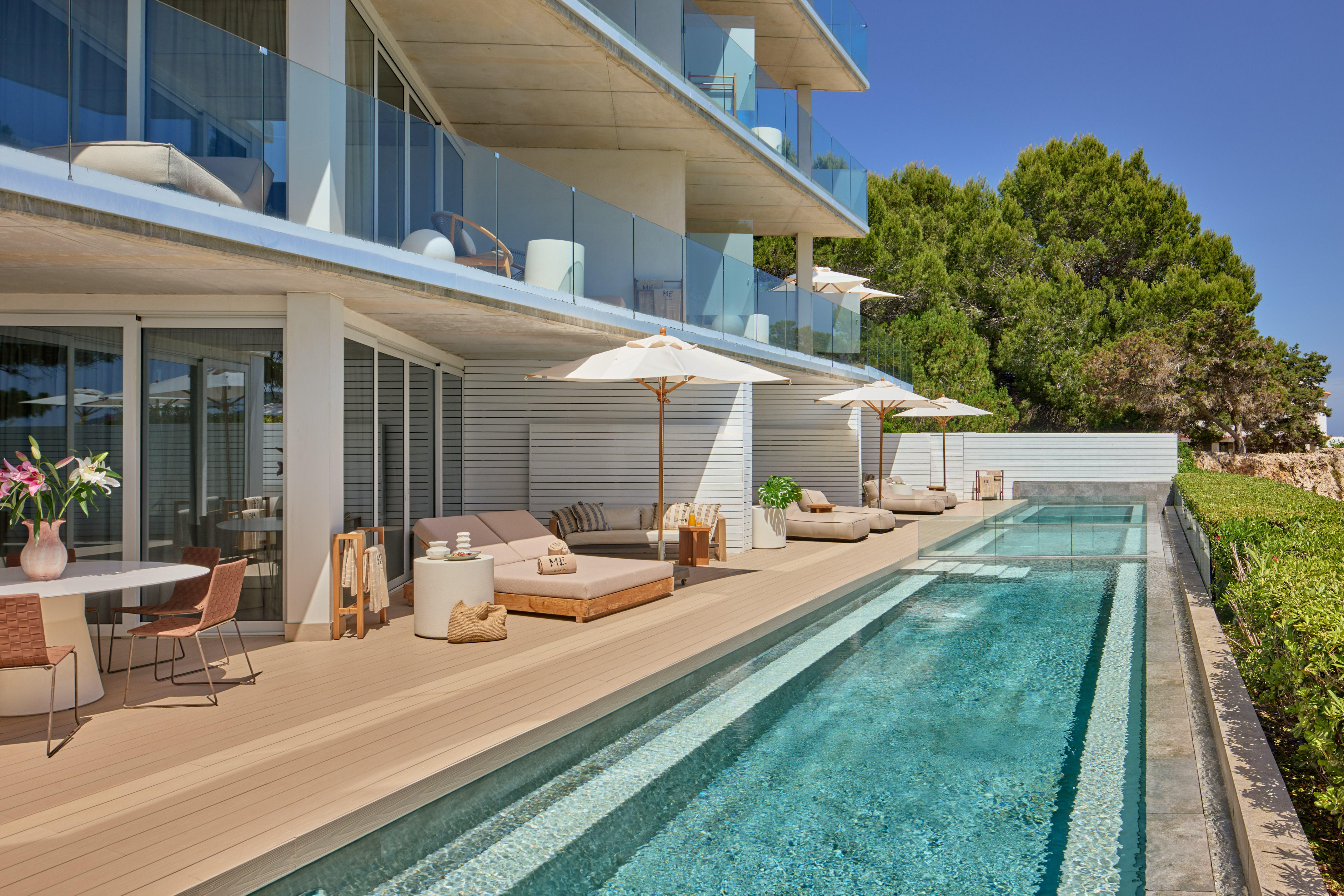 Modern hotel pool deck with sun loungers, private balconies, and lush trees.