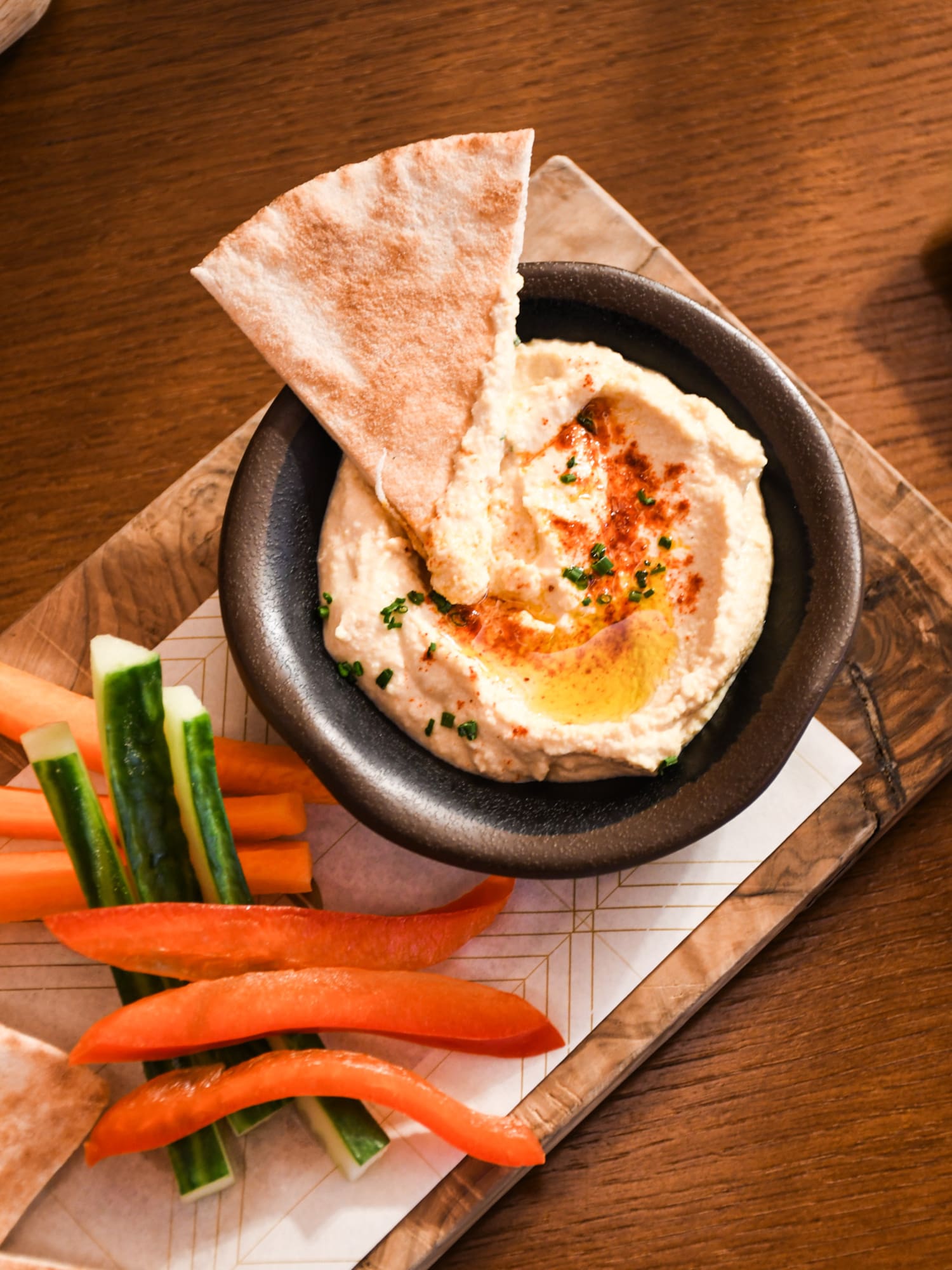 a bowl of hummus and vegetables on a wooden tray