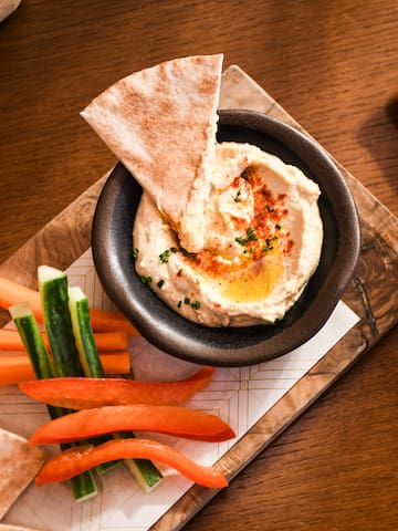 a bowl of hummus and vegetables on a wooden tray