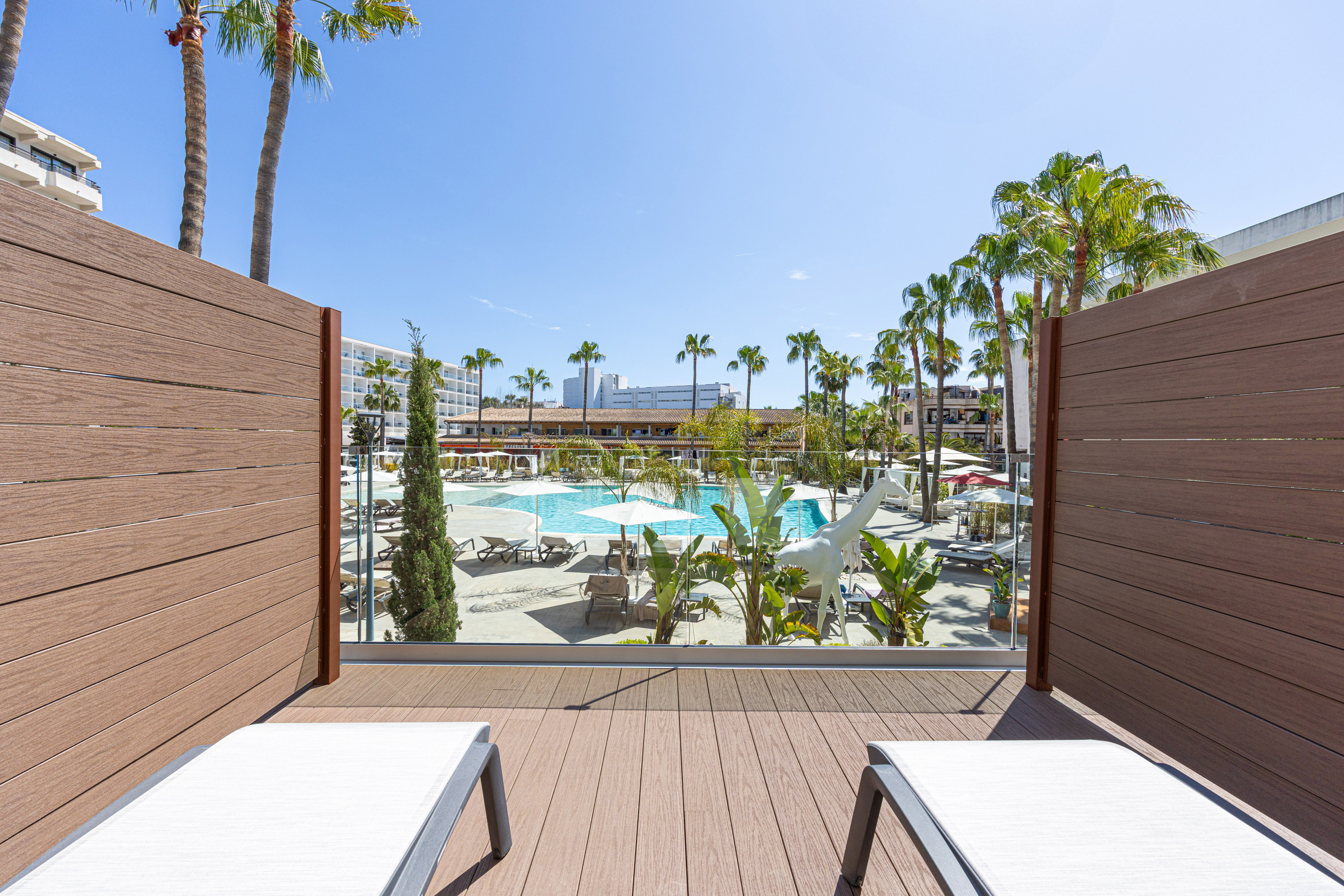Balcony view of hotel resort pool, palm trees, and sun loungers.