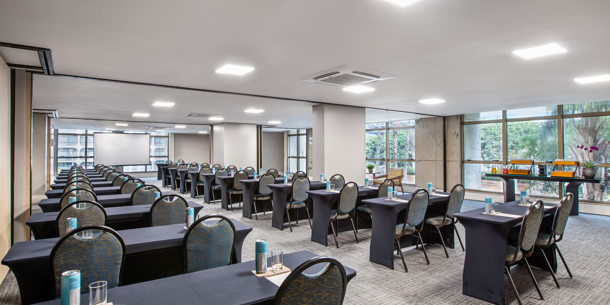 Hotel conference room setup with tables, chairs, projection screen, and natural light.