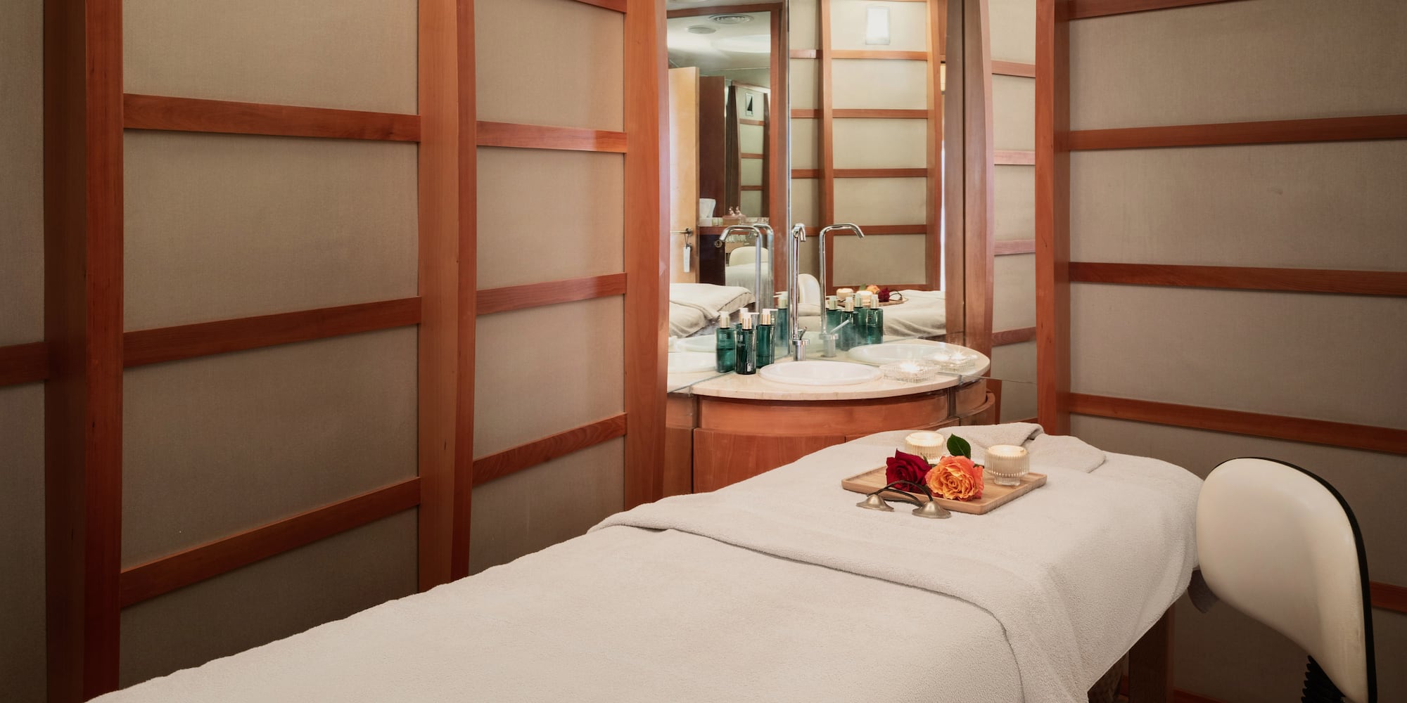 Spa treatment room with massage bed, flowers, and vanity area.