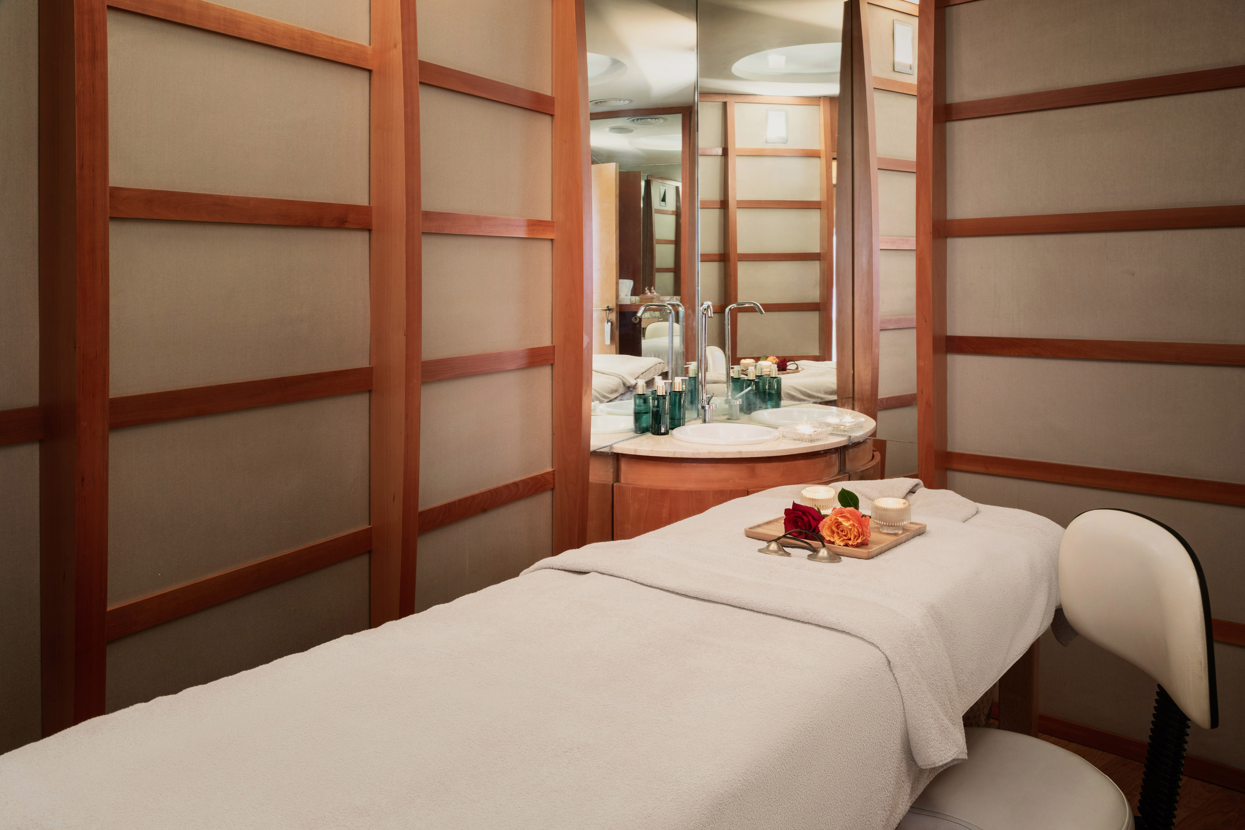 Spa treatment room with massage bed, flowers, and vanity area.