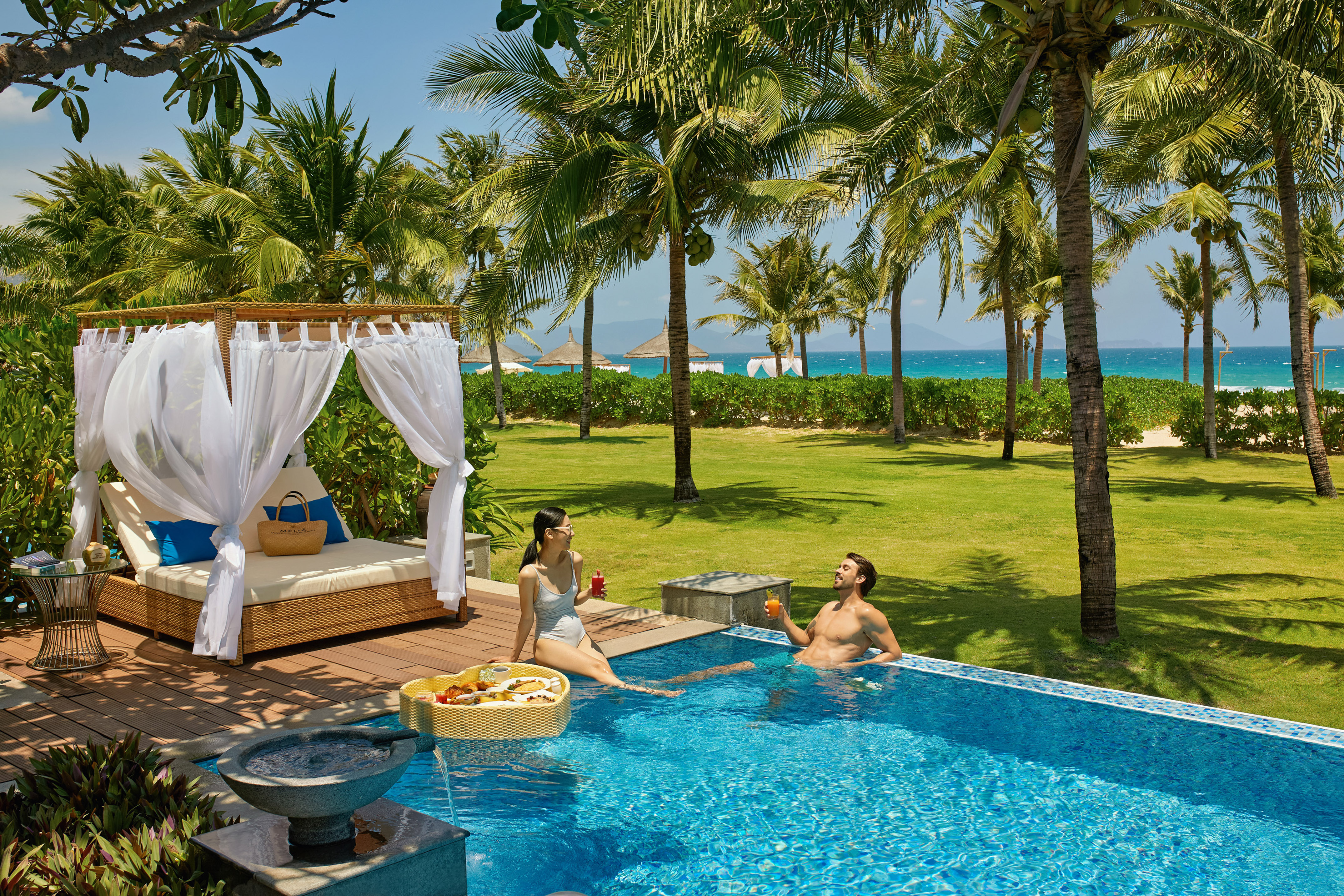 Luxury resort: couple in pool, floating breakfast, palm trees, ocean view.