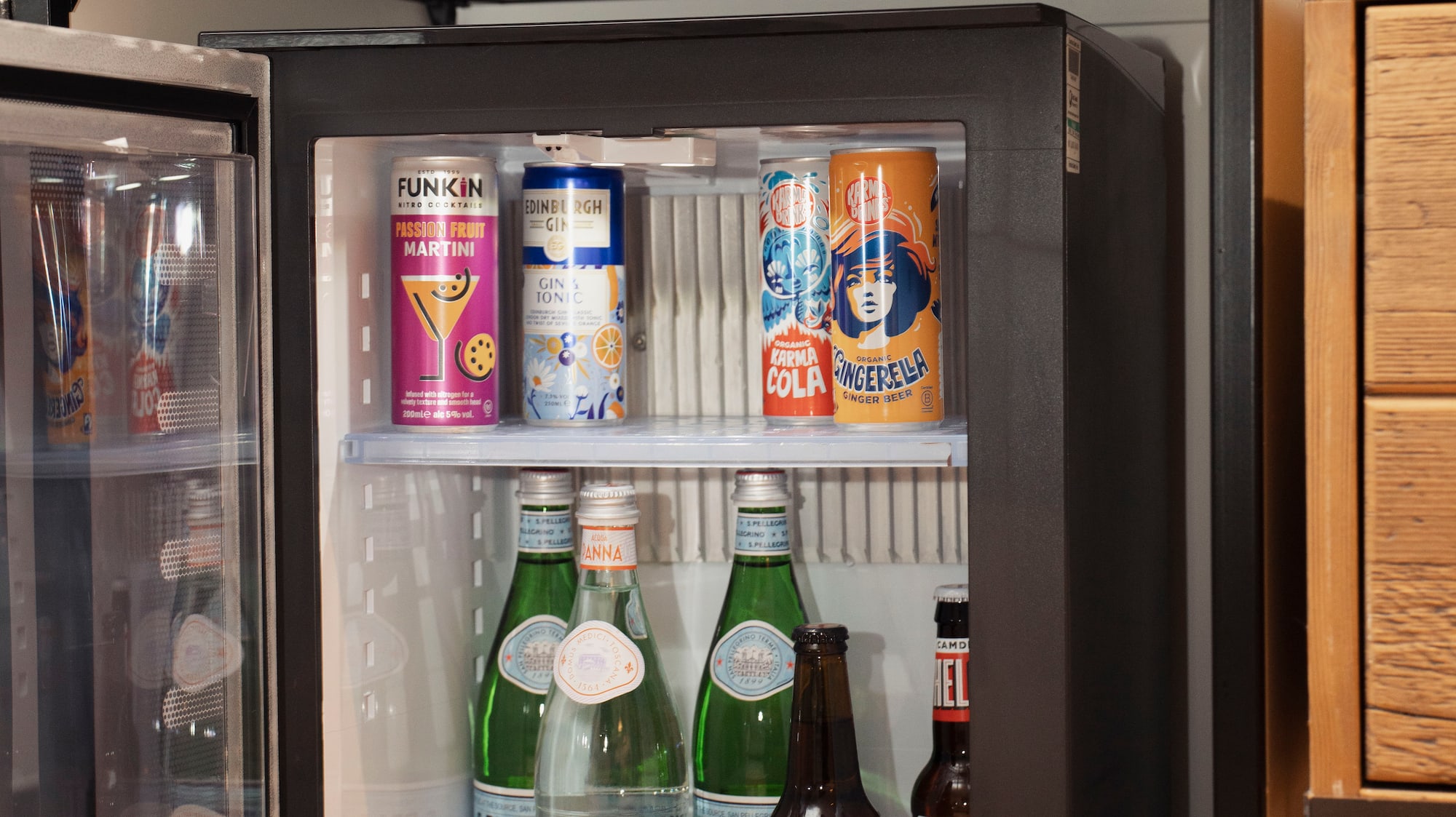 Hotel mini-bar with open fridge stocked with various drinks and Nespresso coffee machine.