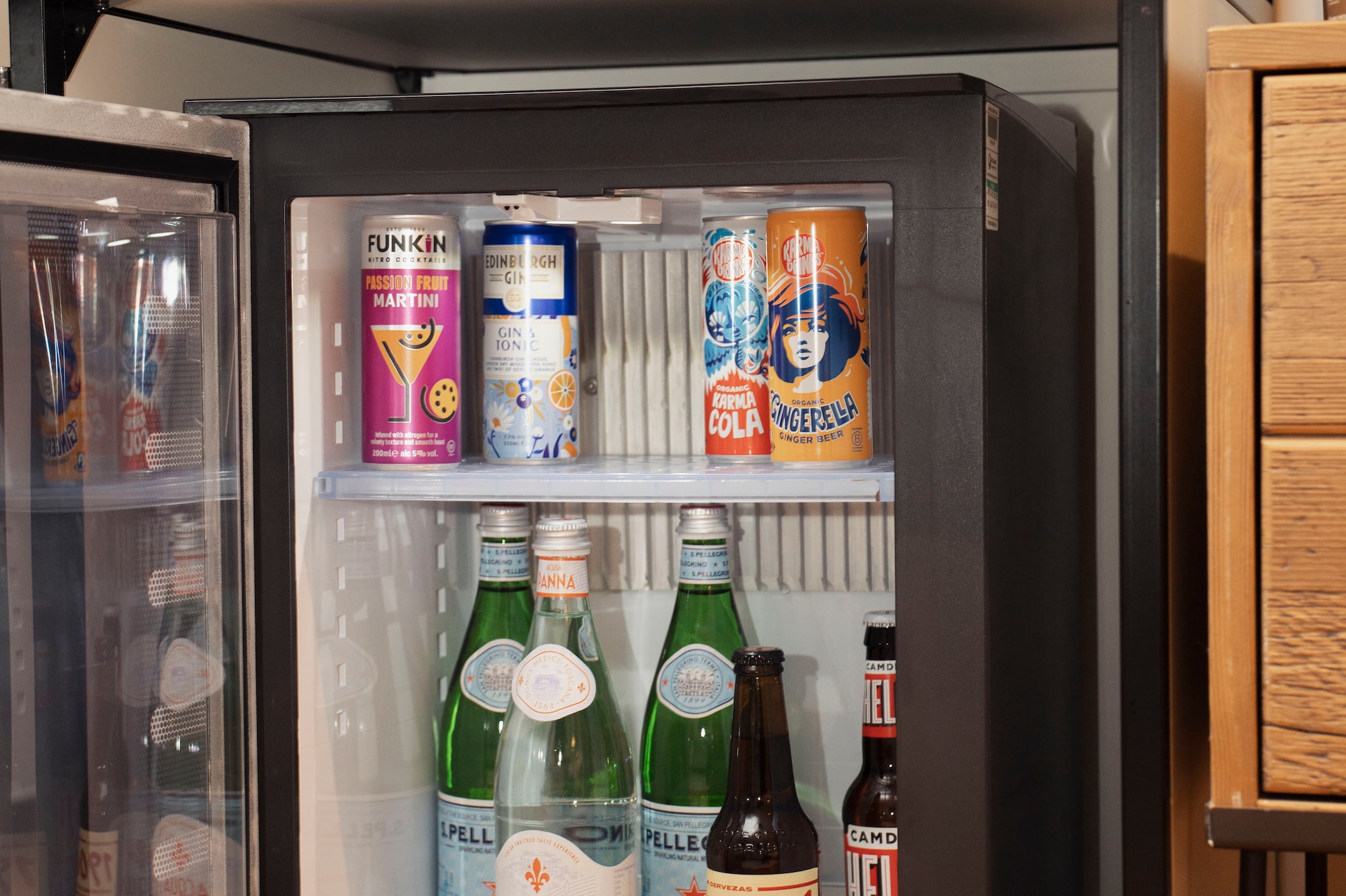 Hotel mini-bar with open fridge stocked with various drinks and Nespresso coffee machine.