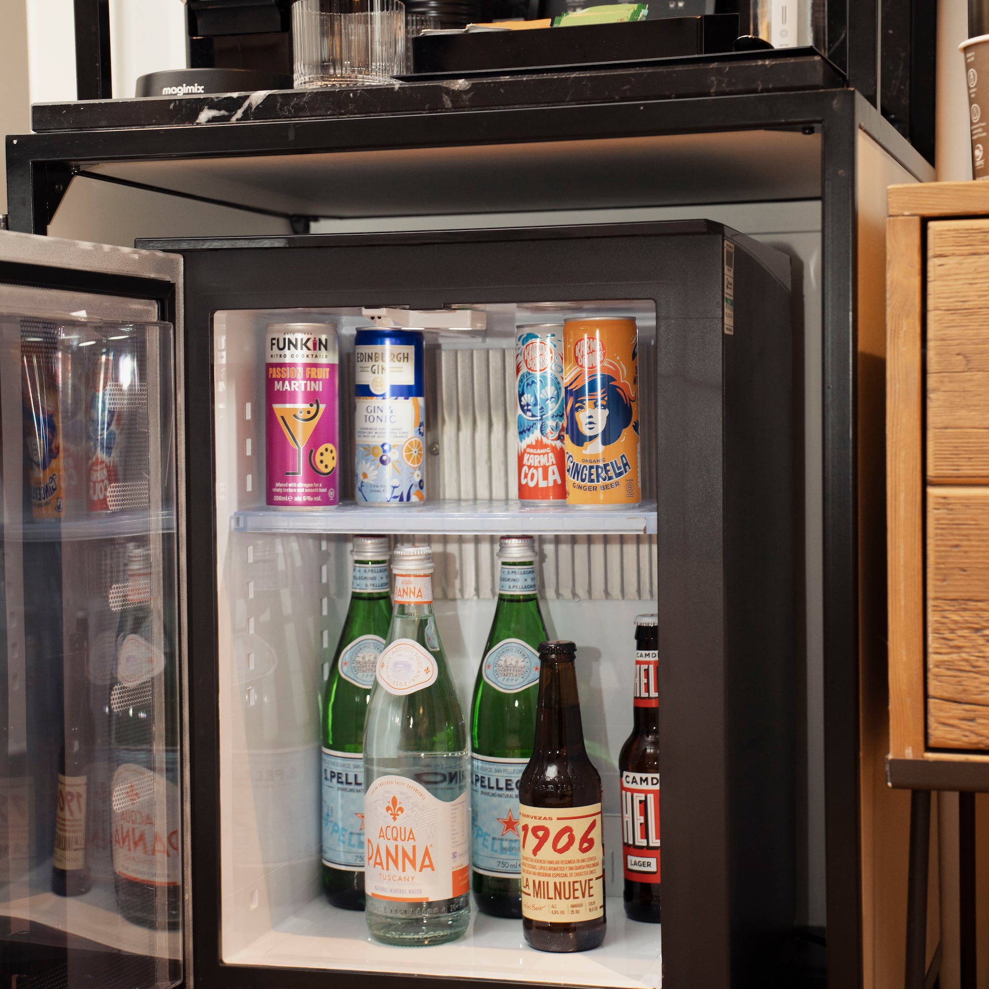 Hotel mini-bar with open fridge stocked with various drinks and Nespresso coffee machine.