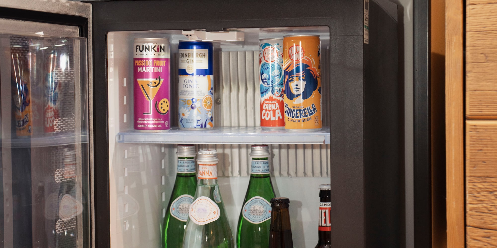Hotel mini-bar with open fridge stocked with various drinks and Nespresso coffee machine.