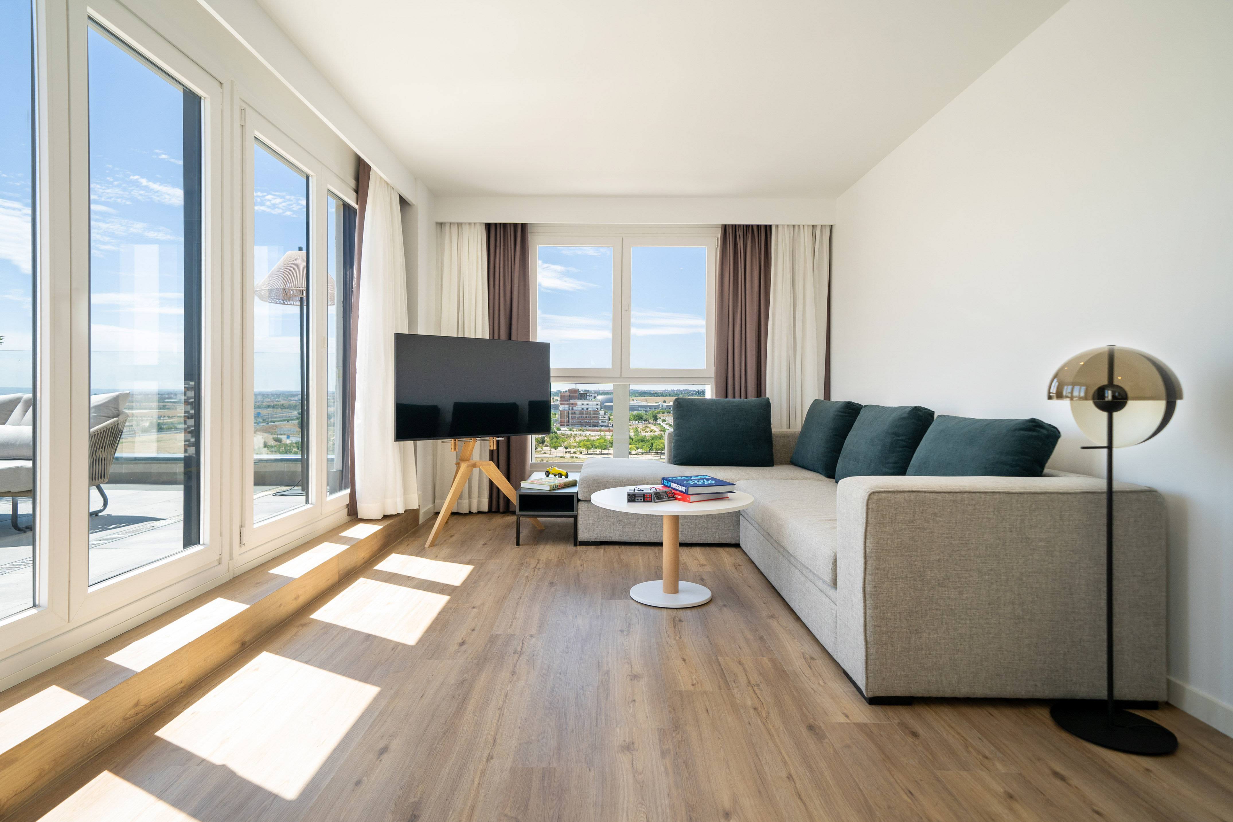 Bright living room with modern sofa, TV, wood floor, and balcony city view.