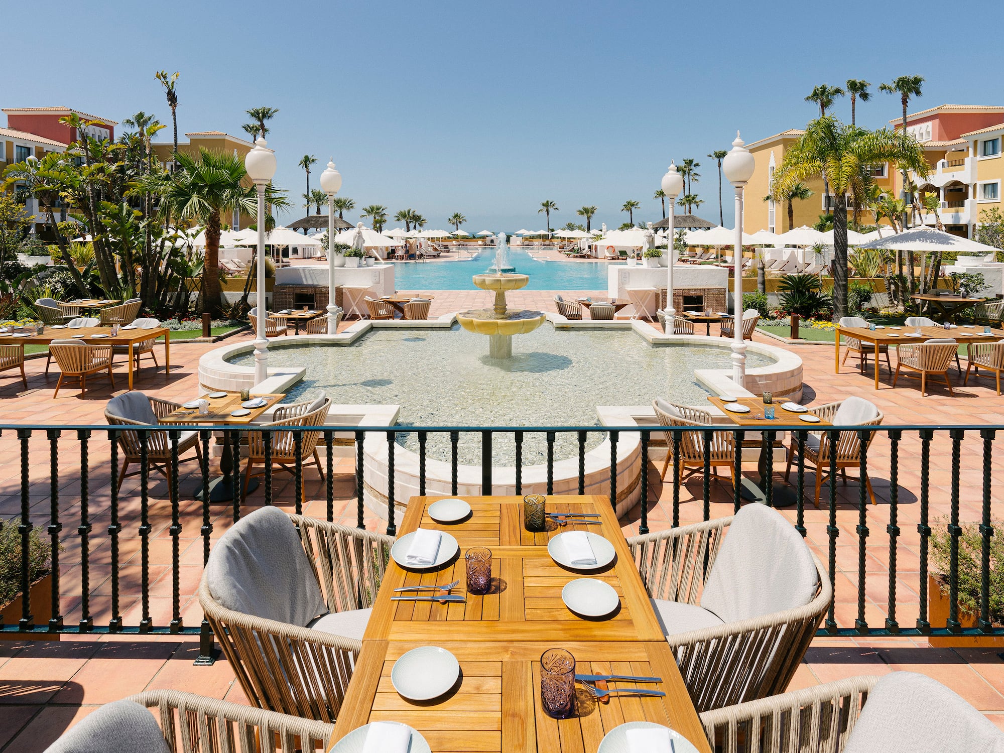 a table and chairs outside with a fountain and palm trees