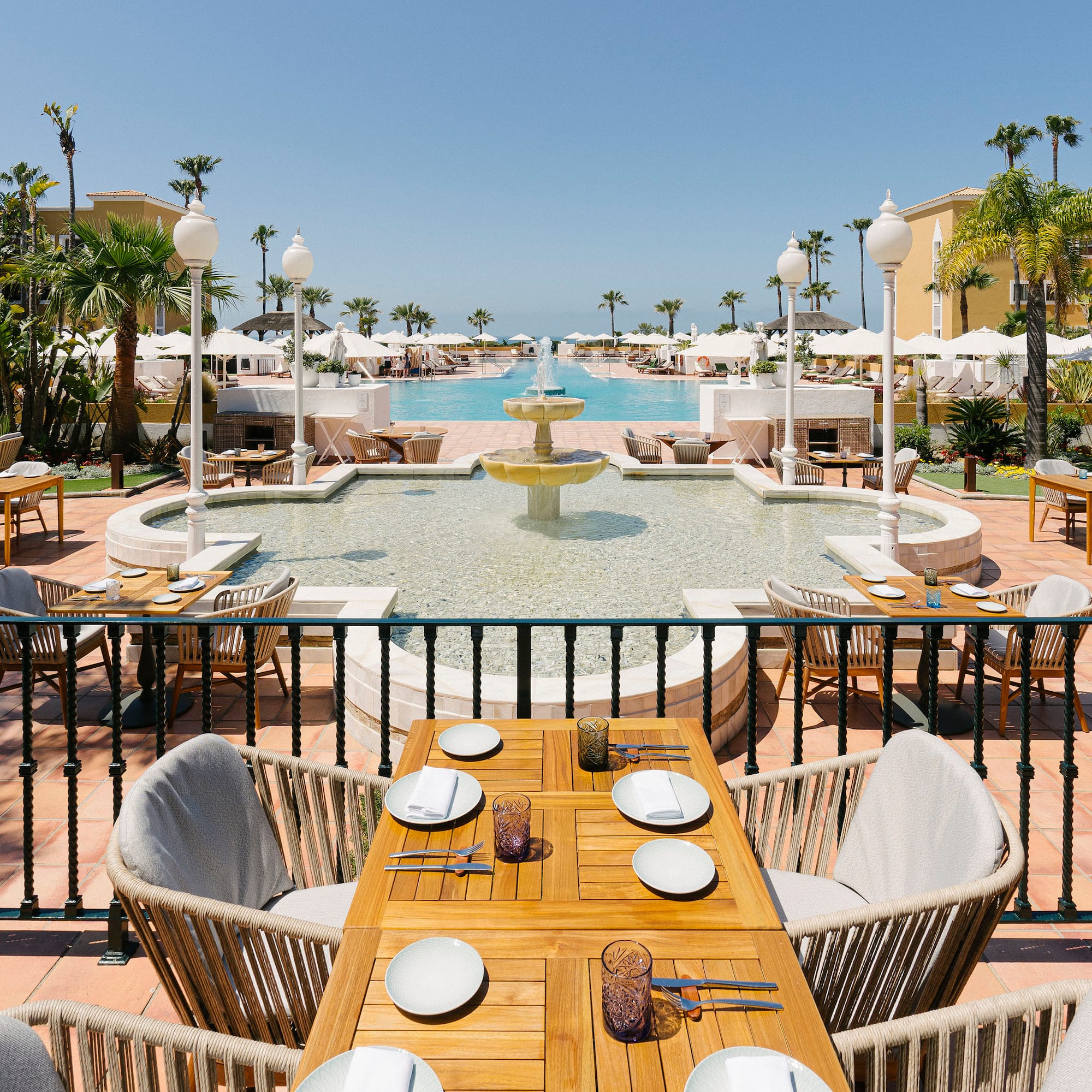 a table and chairs outside with a fountain and palm trees
