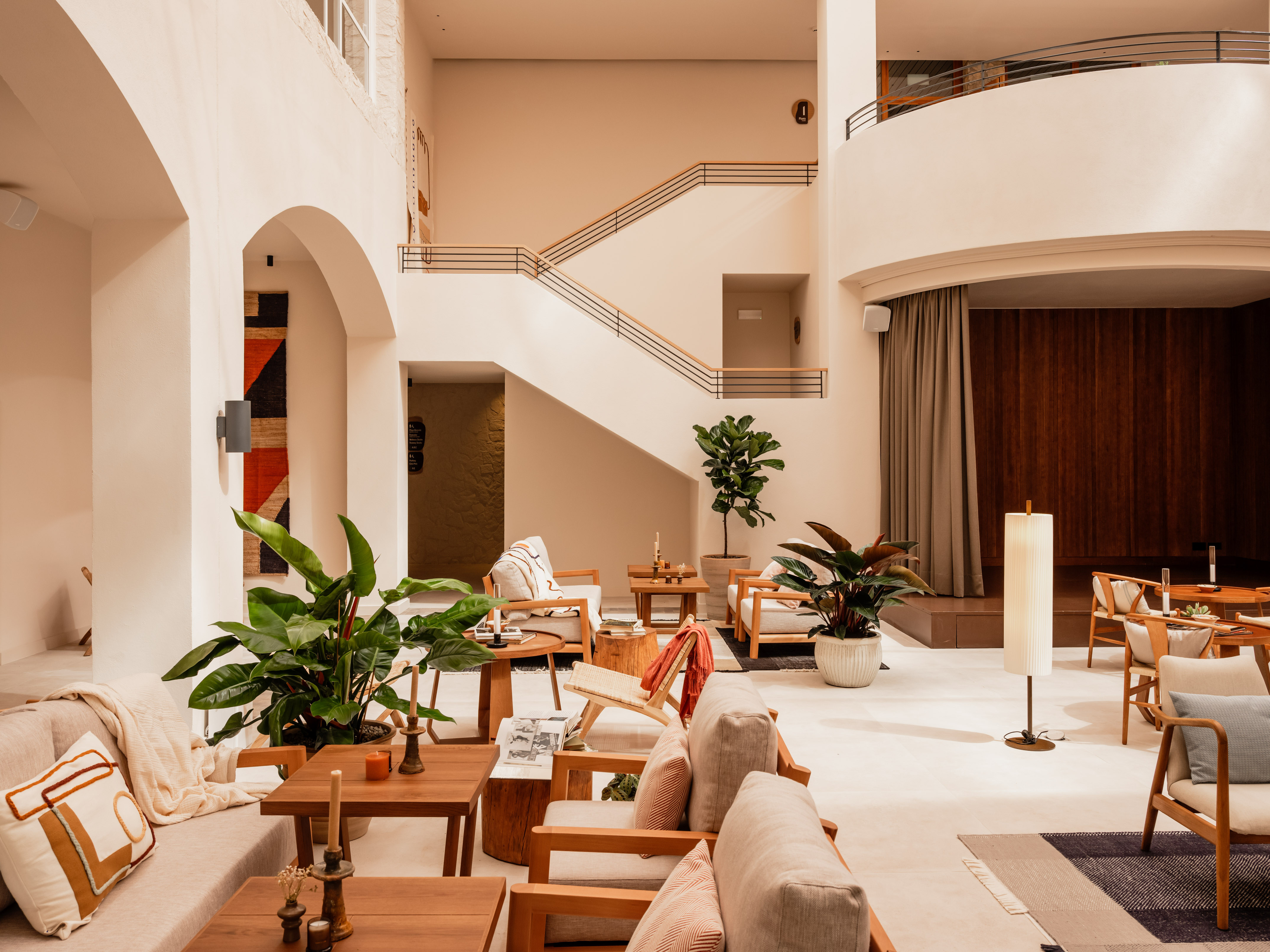 Modern hotel lobby lounge with wooden furniture, lush plants, and a grand staircase.