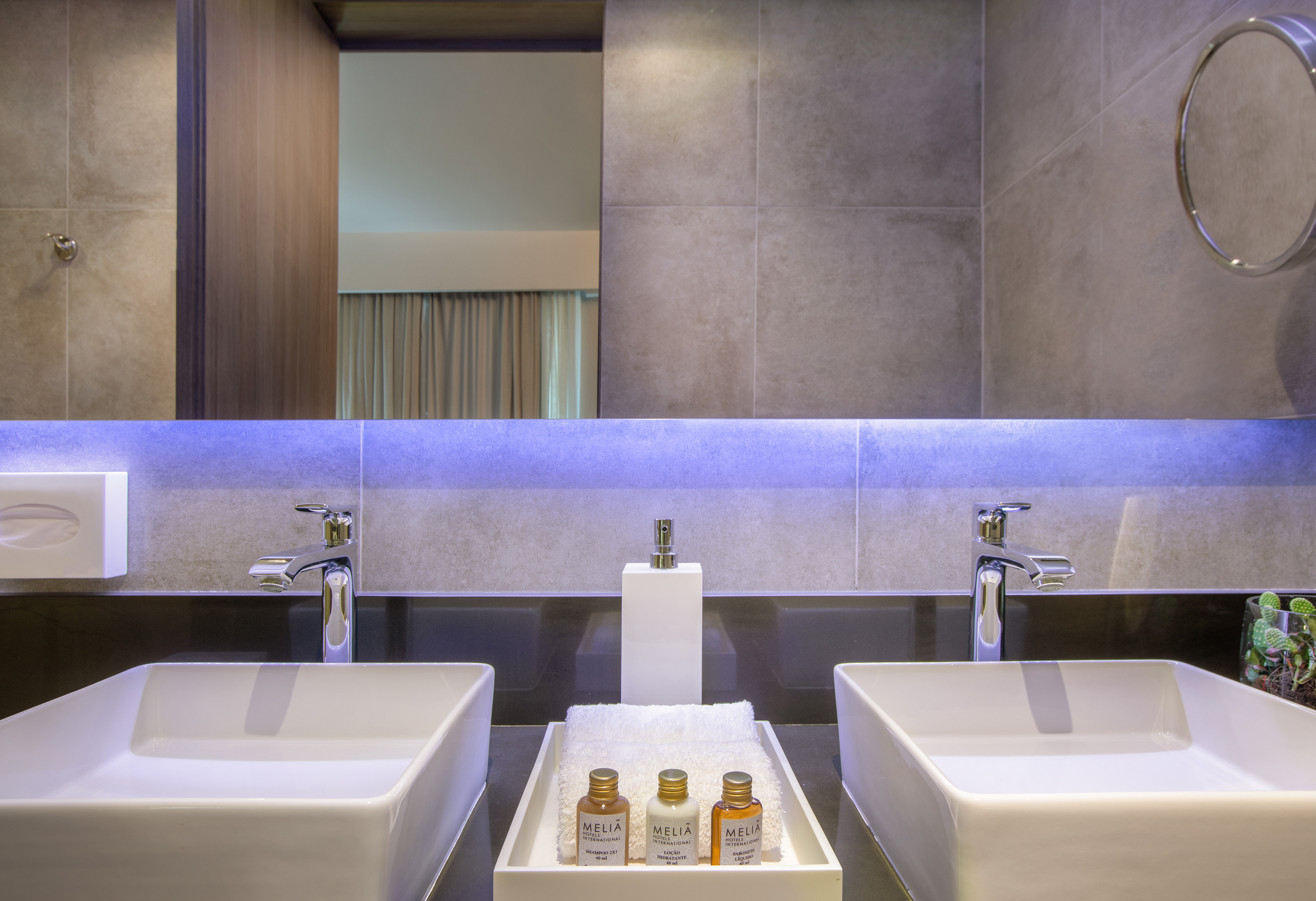 Modern hotel bathroom: dual sinks, backlit mirror with blue light, Meliá toiletries.