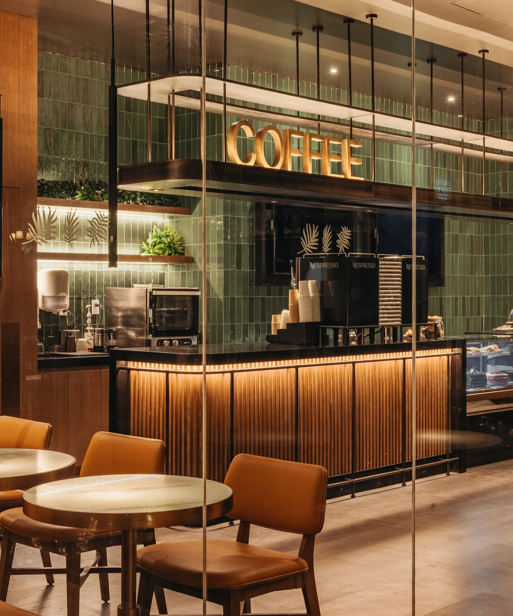 Modern coffee shop with "COFFEE" sign, green tiles, wood counter, and plant decor.