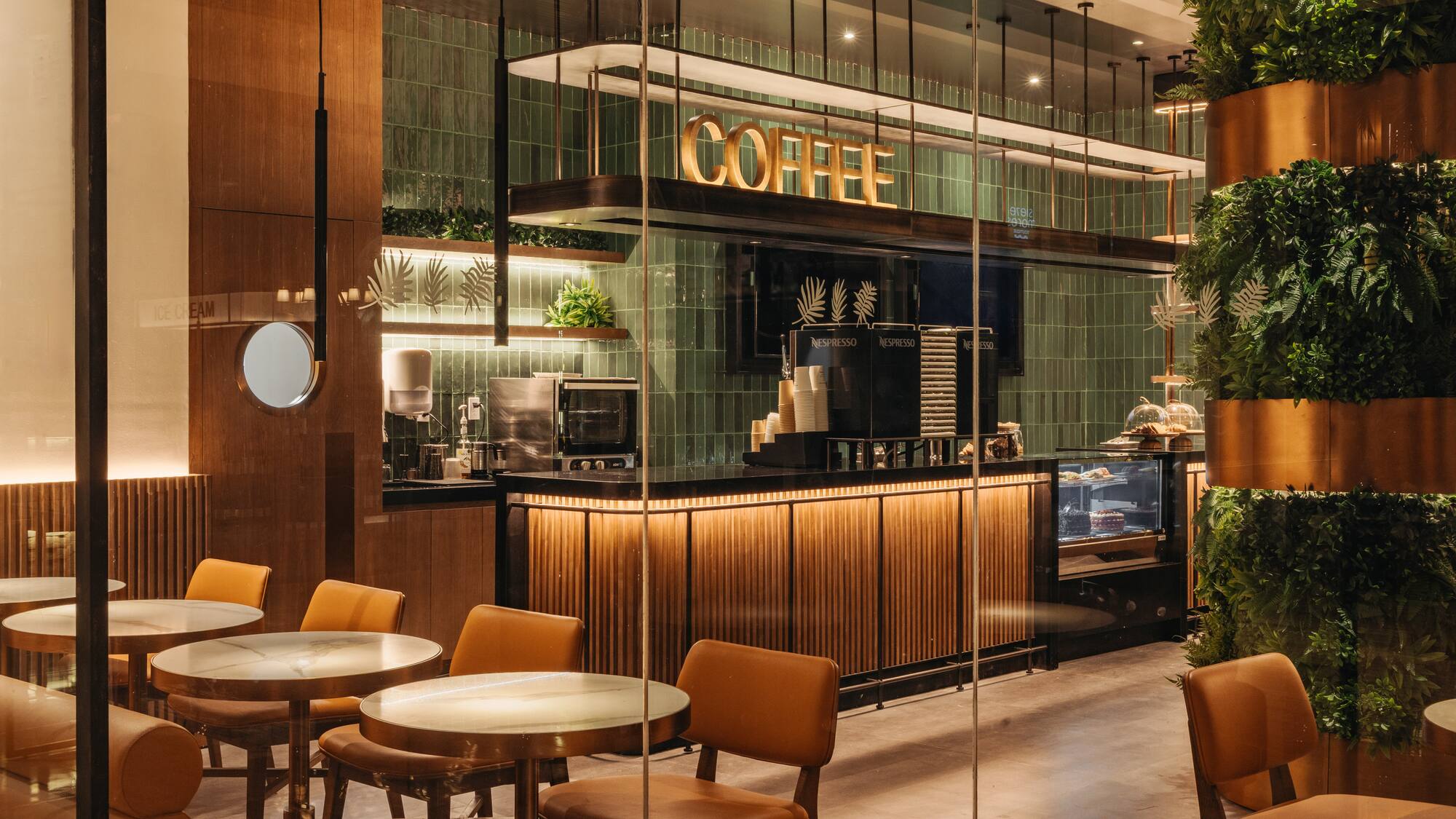 Modern cafe with illuminated COFFEE sign, green tiles, and wood accents.
