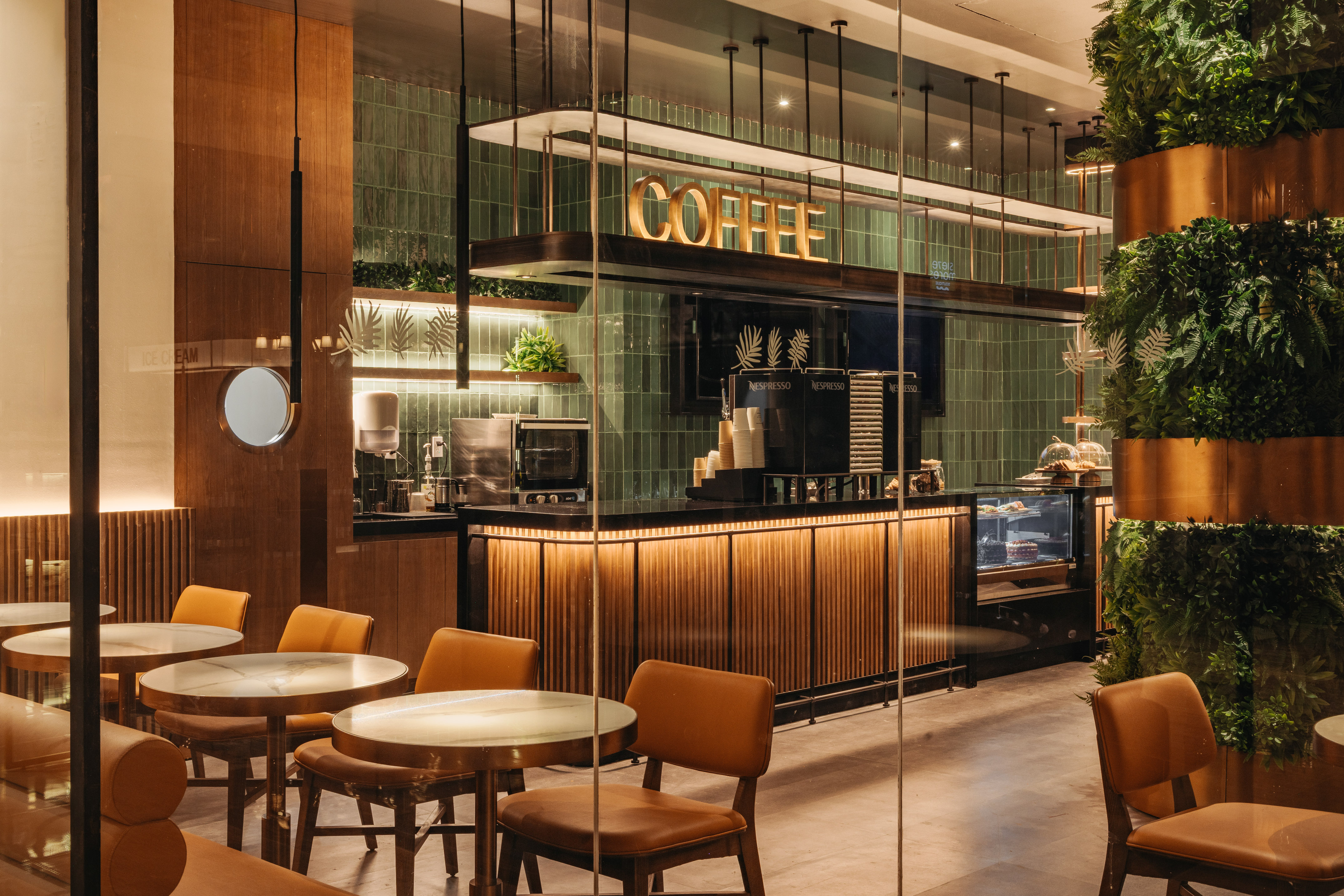 Modern coffee shop with "COFFEE" sign, green tiles, wood counter, and plant decor.