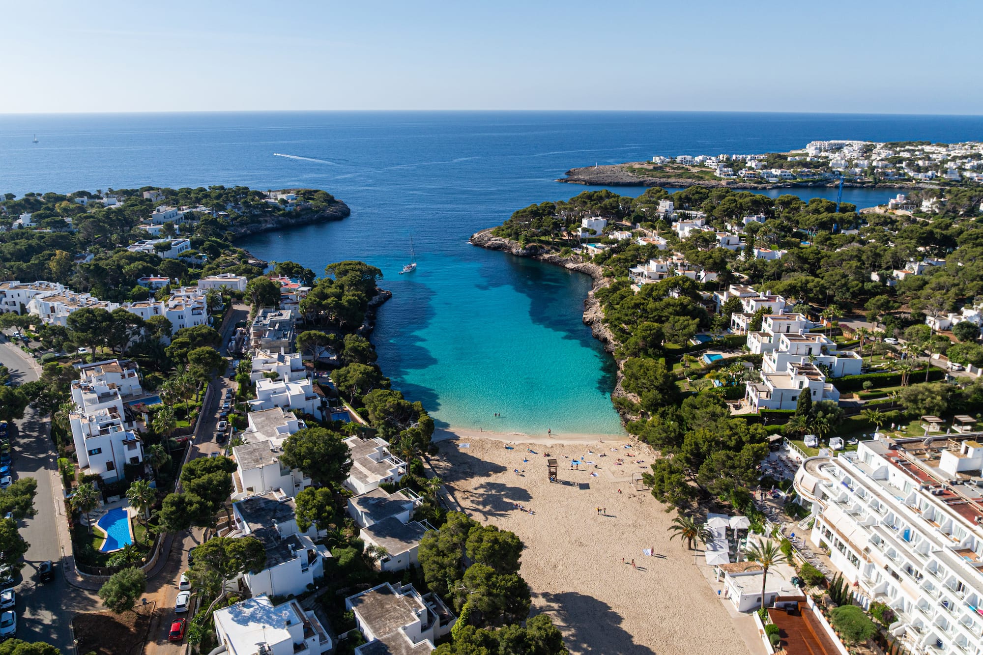 Cala turquesa en Mallorca con playa, villas blancas y pinos.