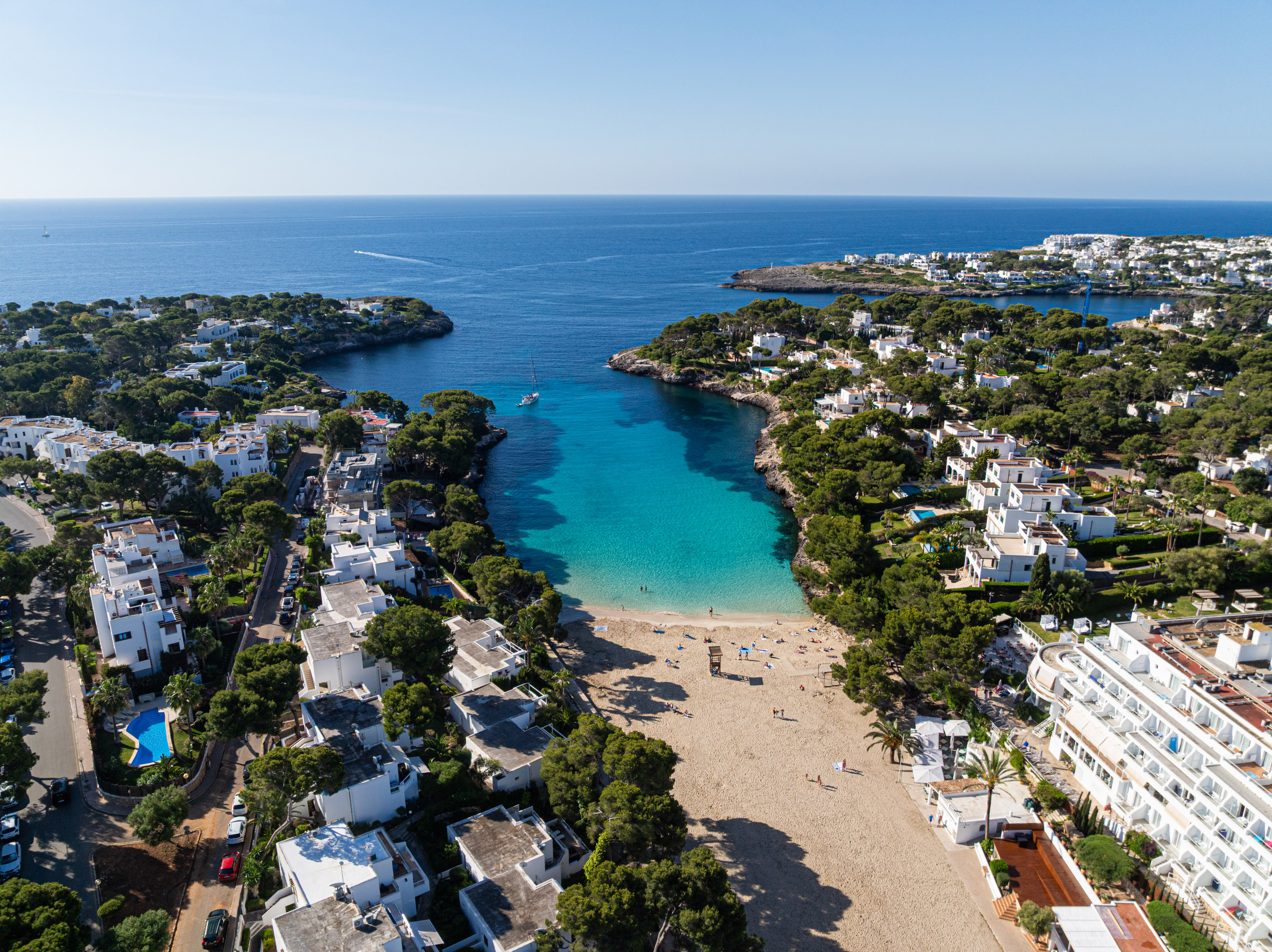 Cala turquesa en Mallorca con playa, villas blancas y pinos.