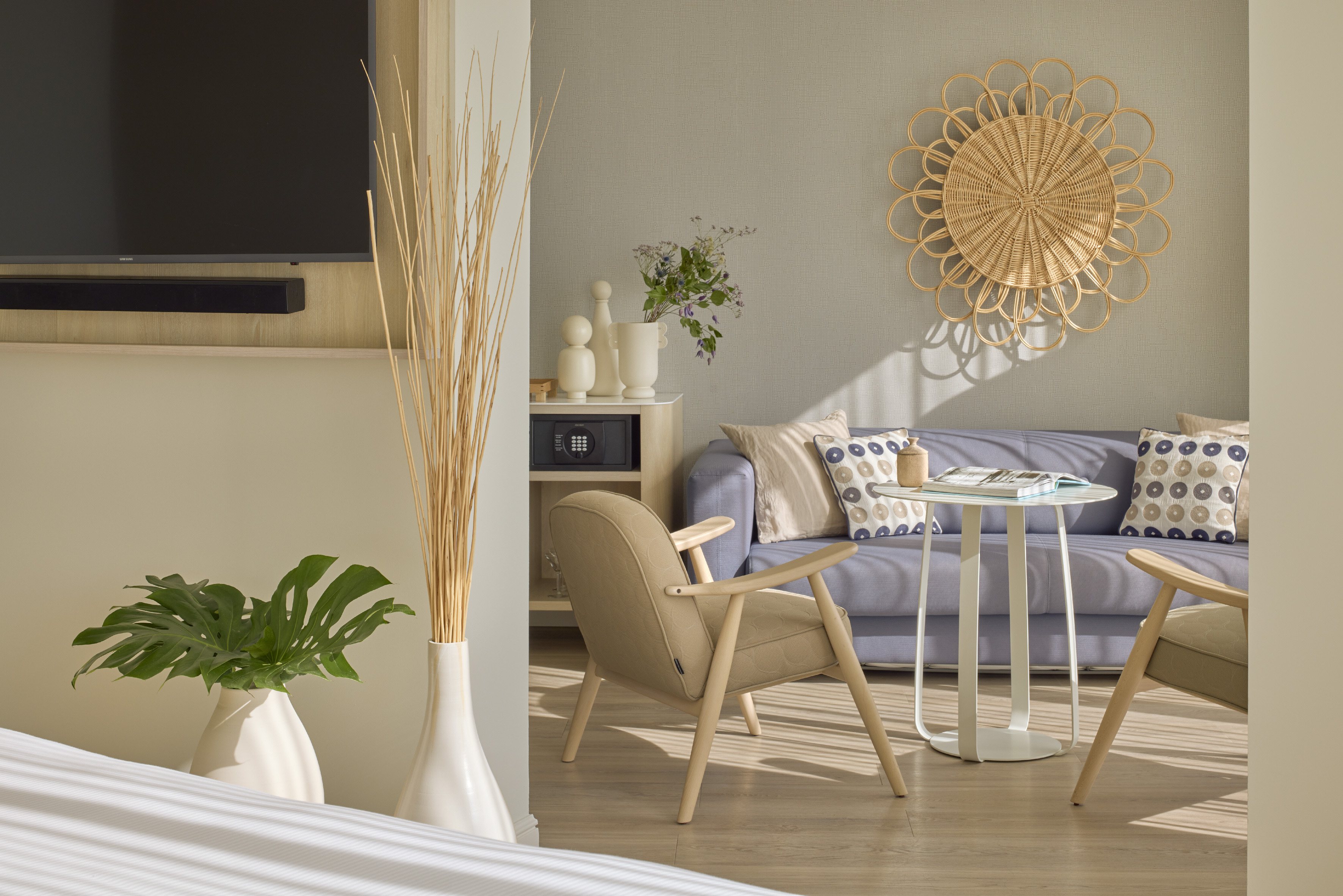 Modern hotel living room with blue sofa, beige armchairs, and rattan wall decor.