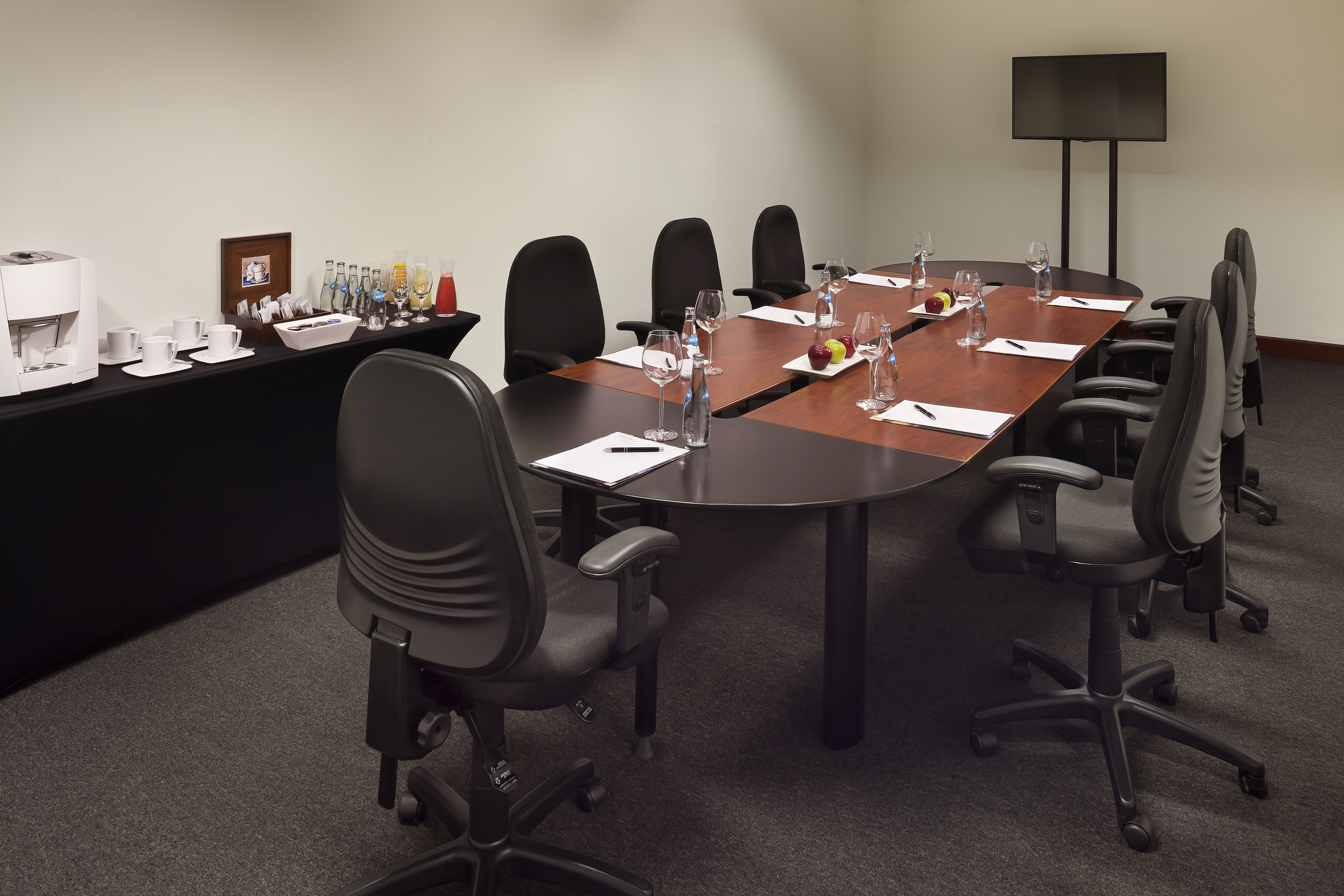 Conference room with large table, office chairs, TV, and refreshment station.