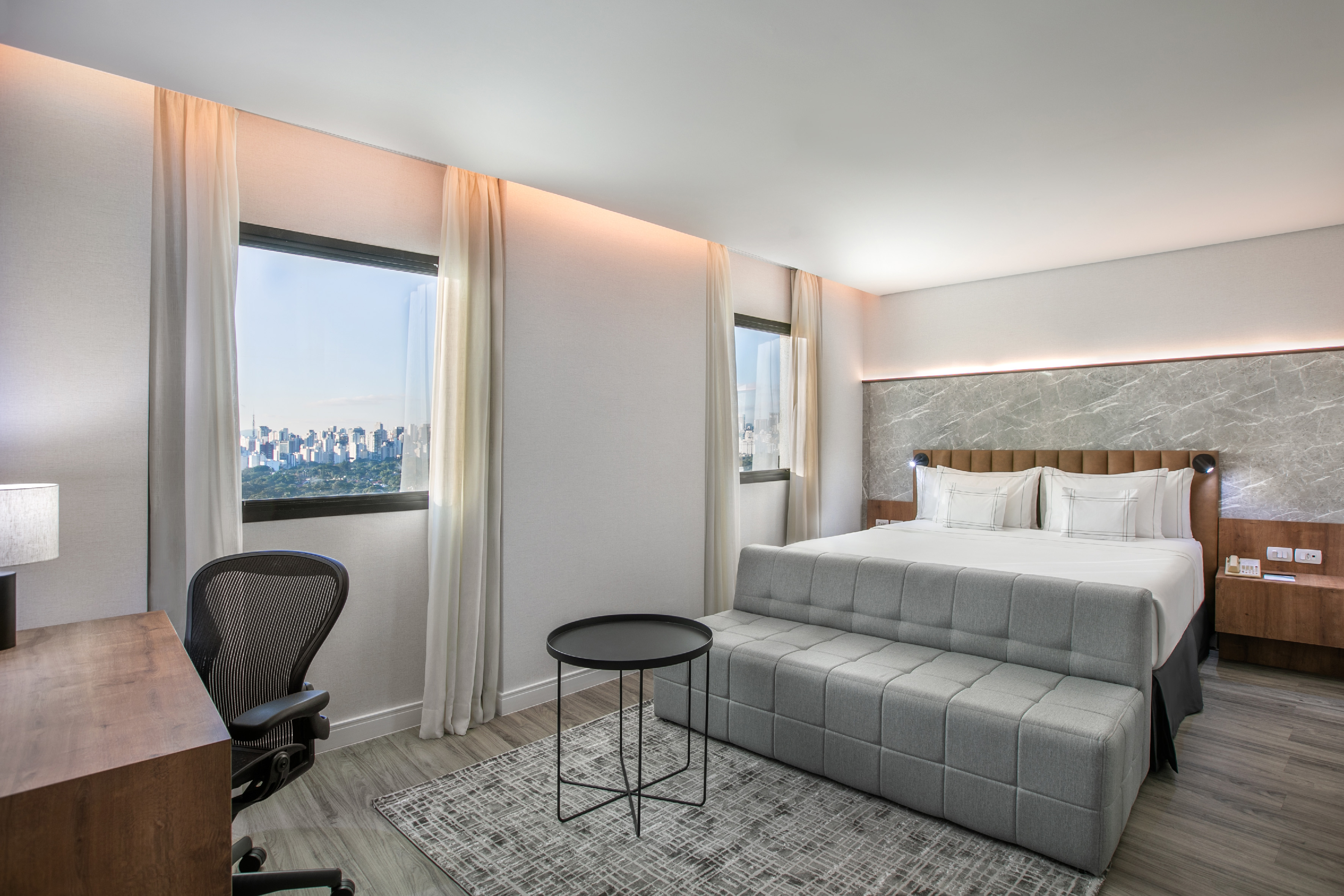 Contemporary hotel bedroom with city skyline view, king bed, and work desk.