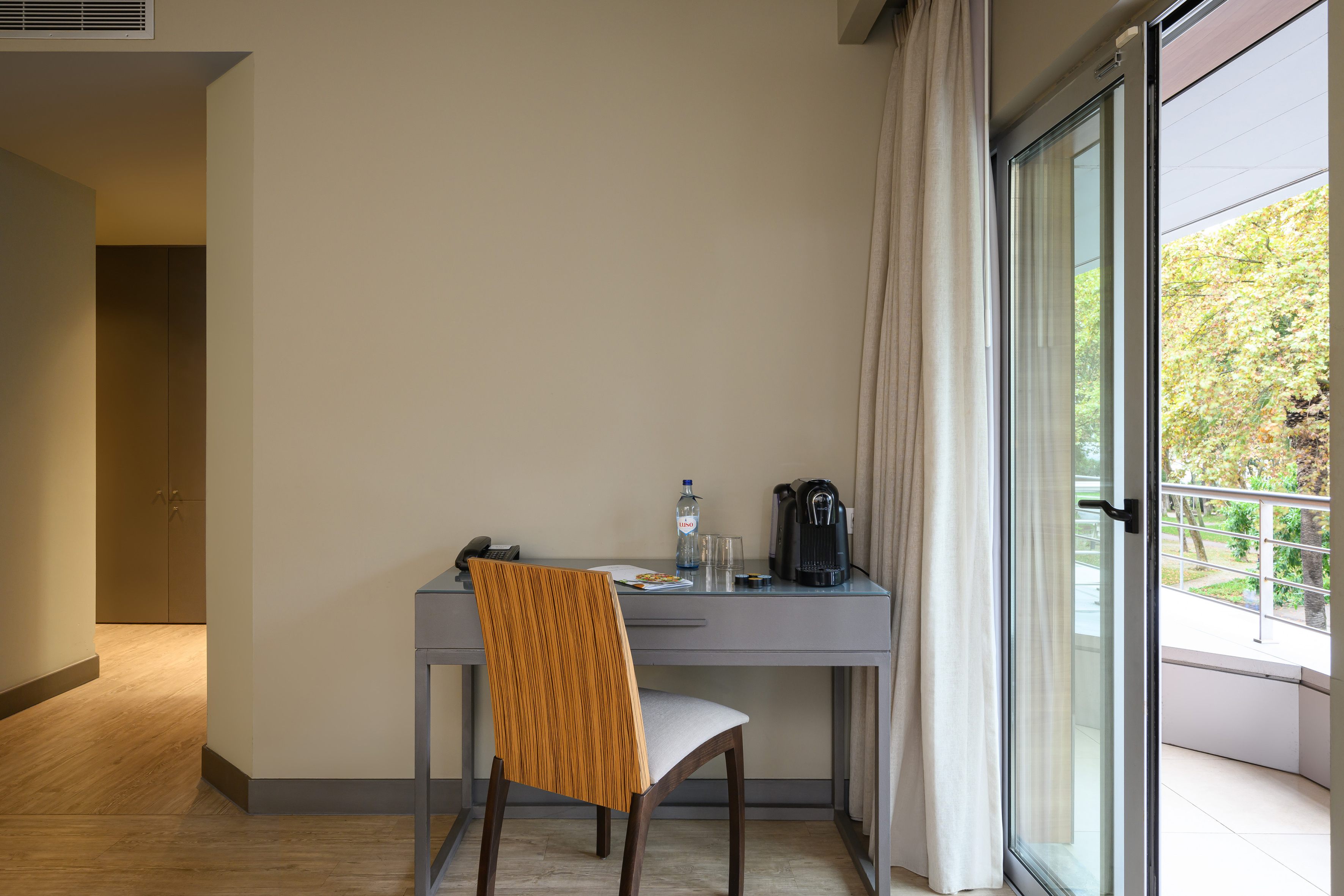 Modern hotel room with work desk, coffee machine, and balcony.