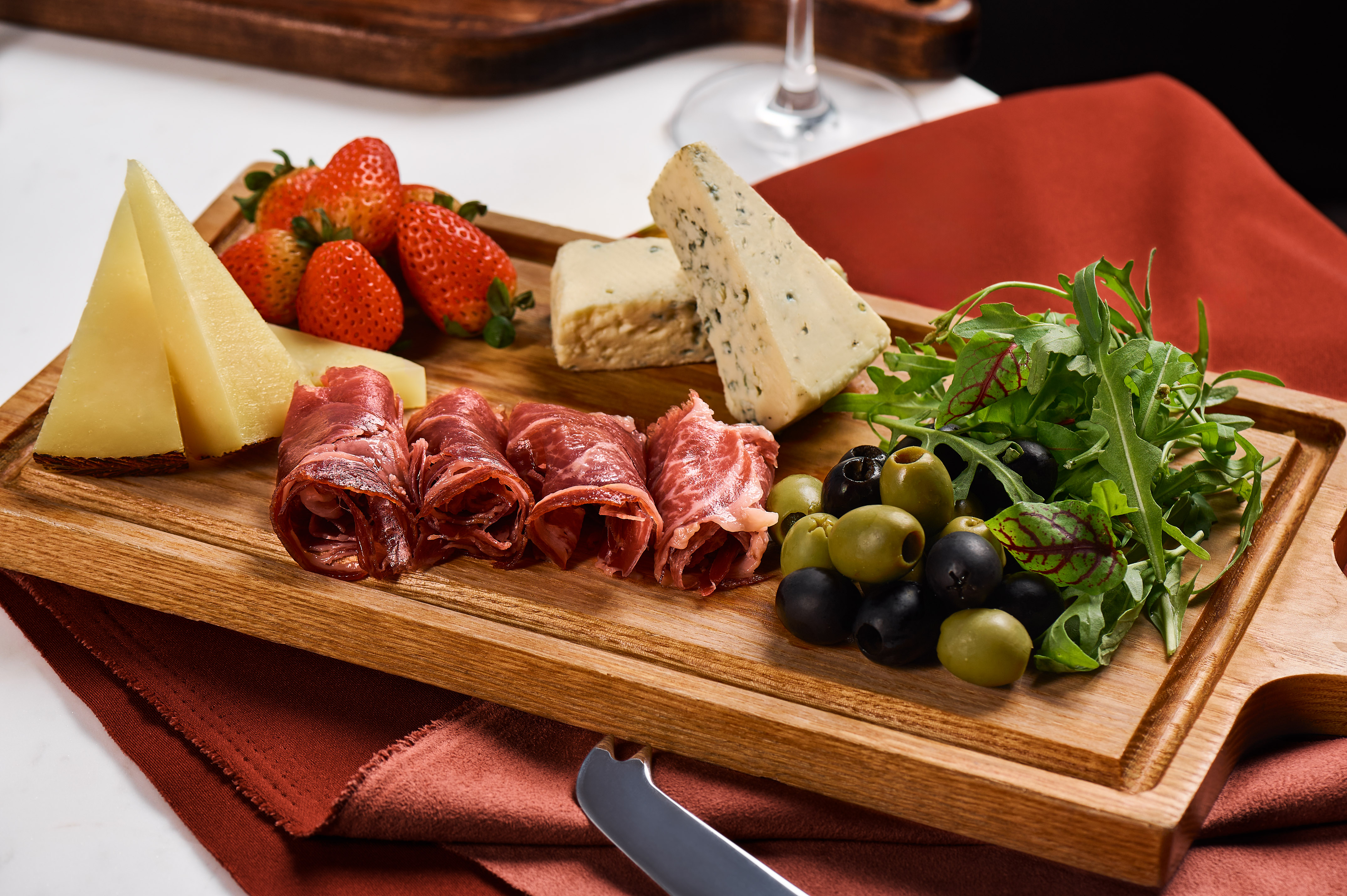 Charcuterie board with cheeses, prosciutto, strawberries, olives, and arugula.
