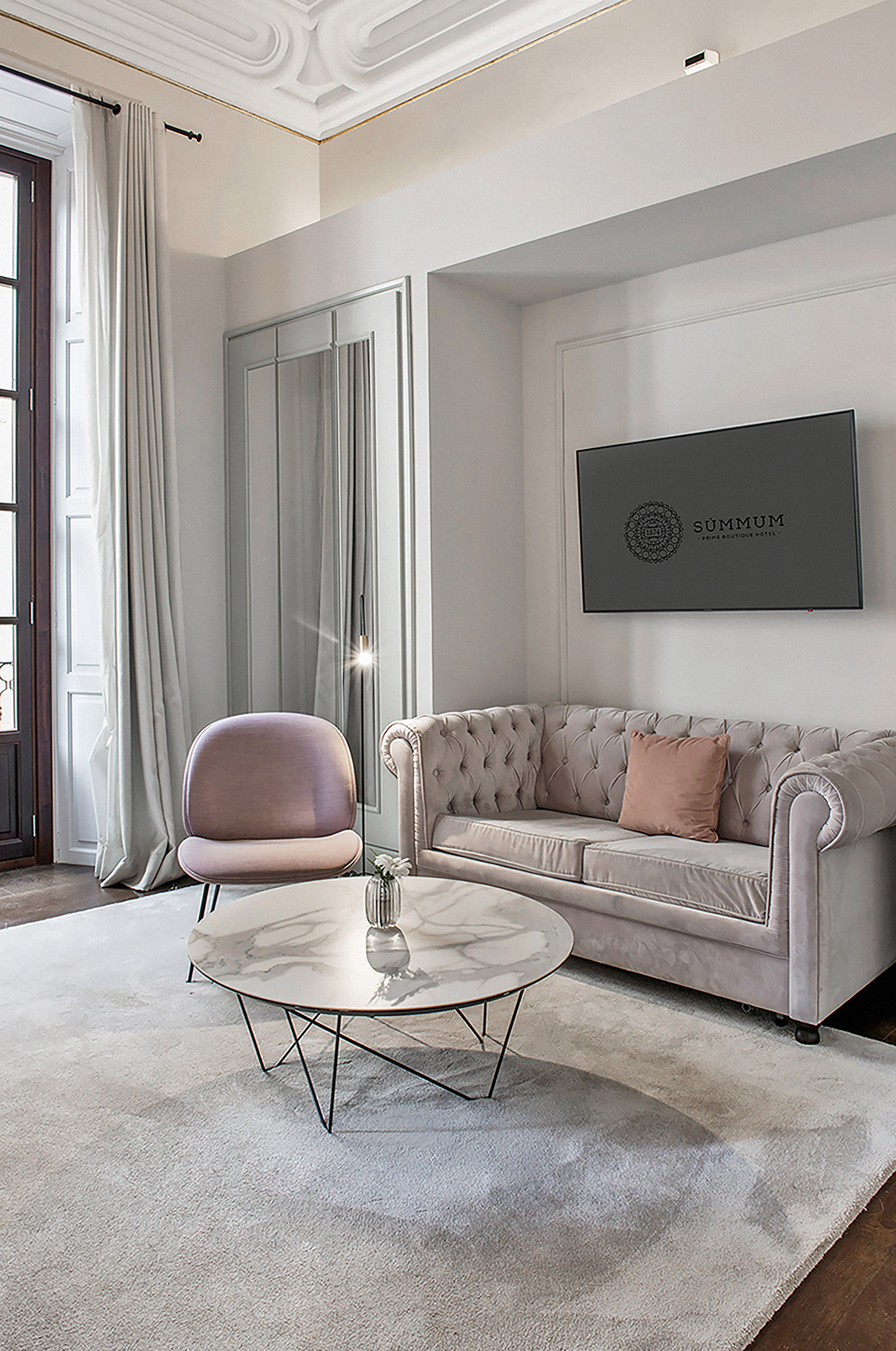 Elegant hotel lounge with tufted sofa, pink chair, marble table, and Summum TV.