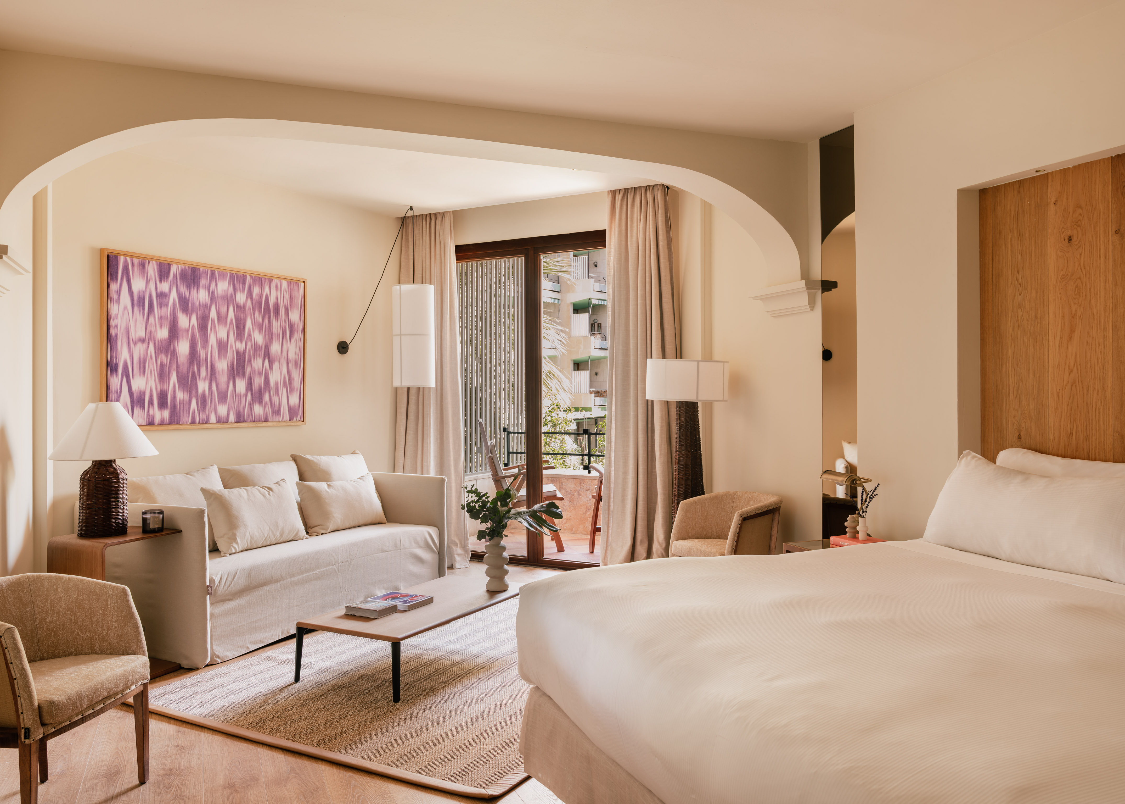 Elegant hotel suite with separate bedroom, living area, archway, and balcony view.