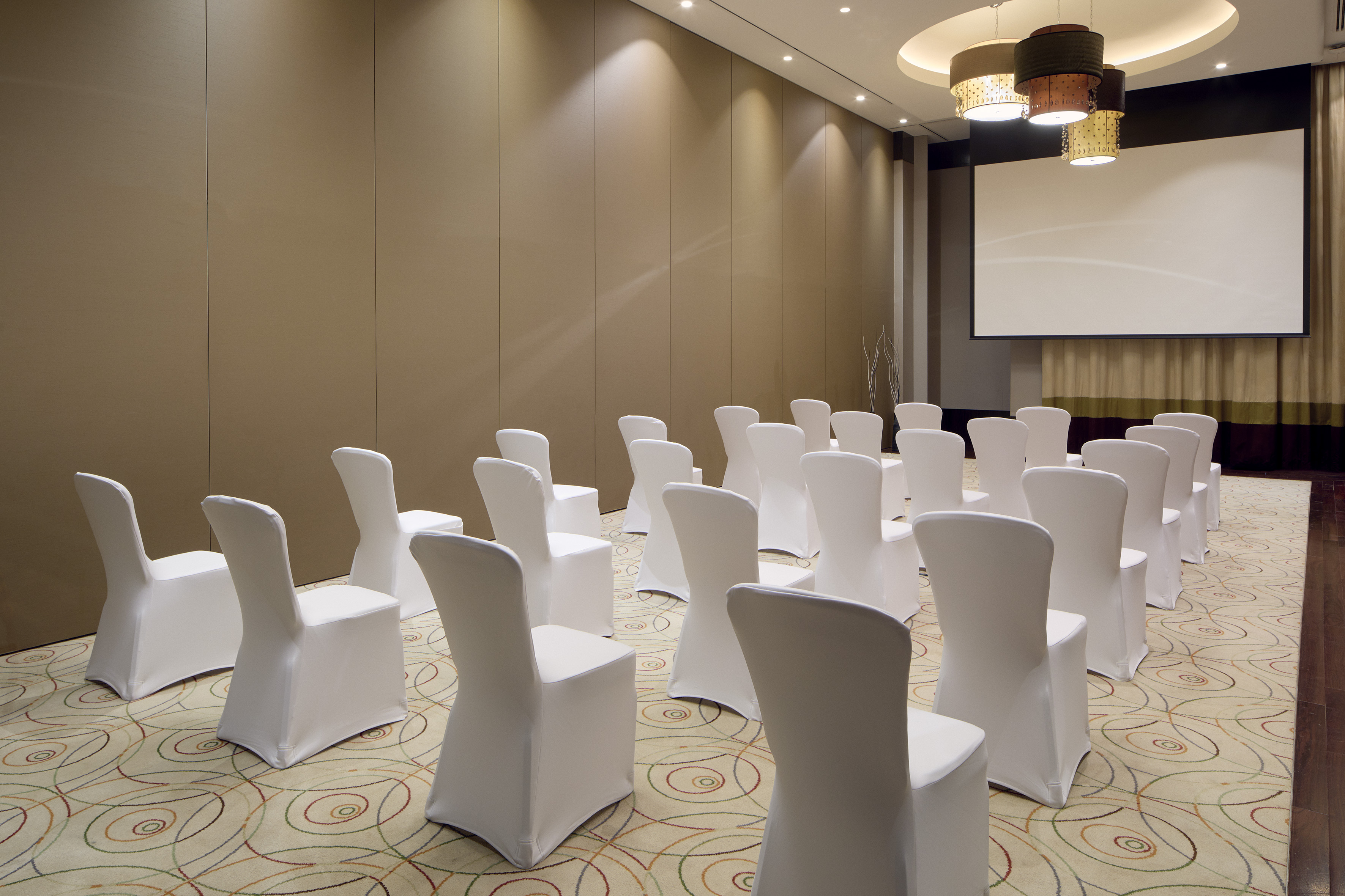 Empty conference room with white chairs, projector screen, and patterned carpet.