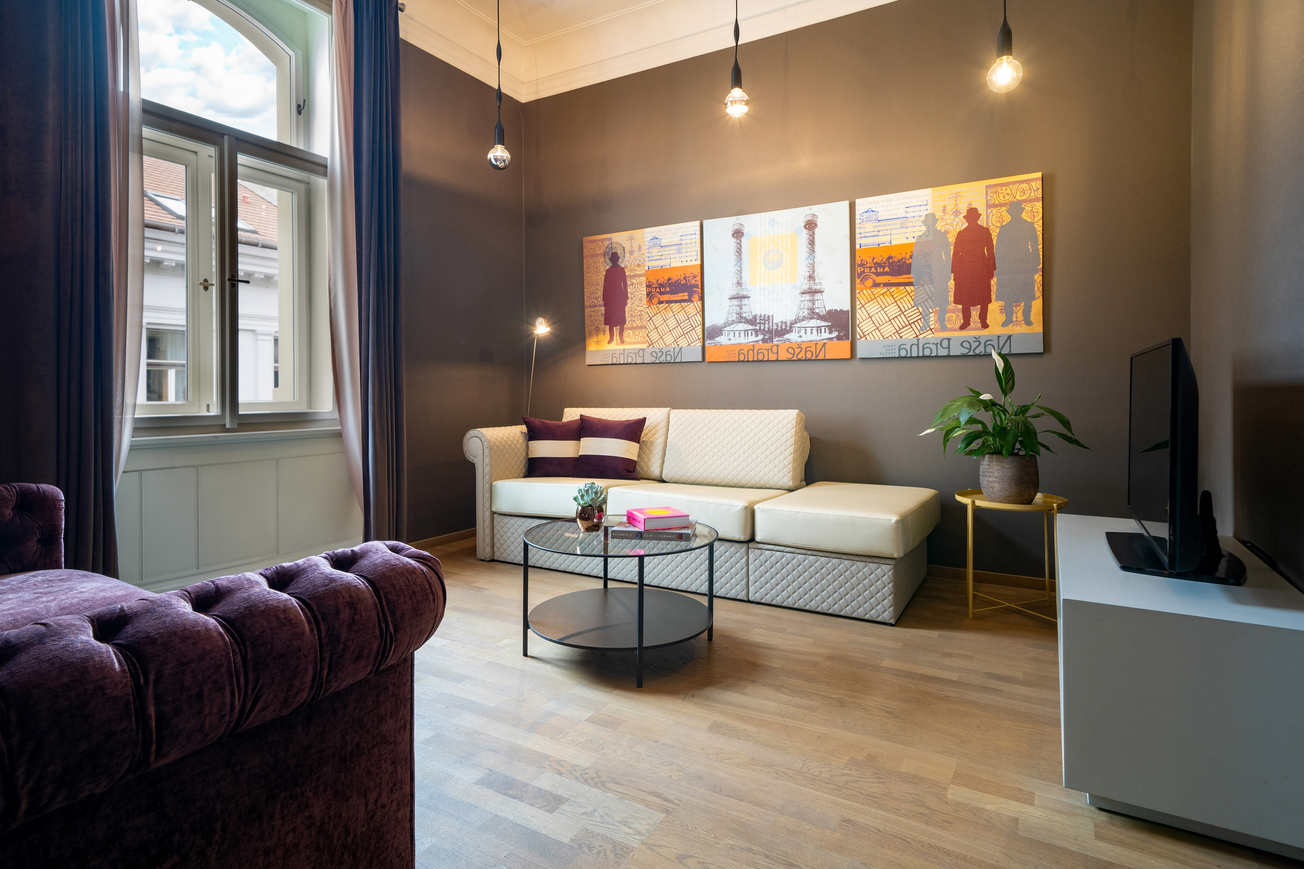 Modern living room with cream sectional, purple velvet sofa, wood floor, and urban art.
