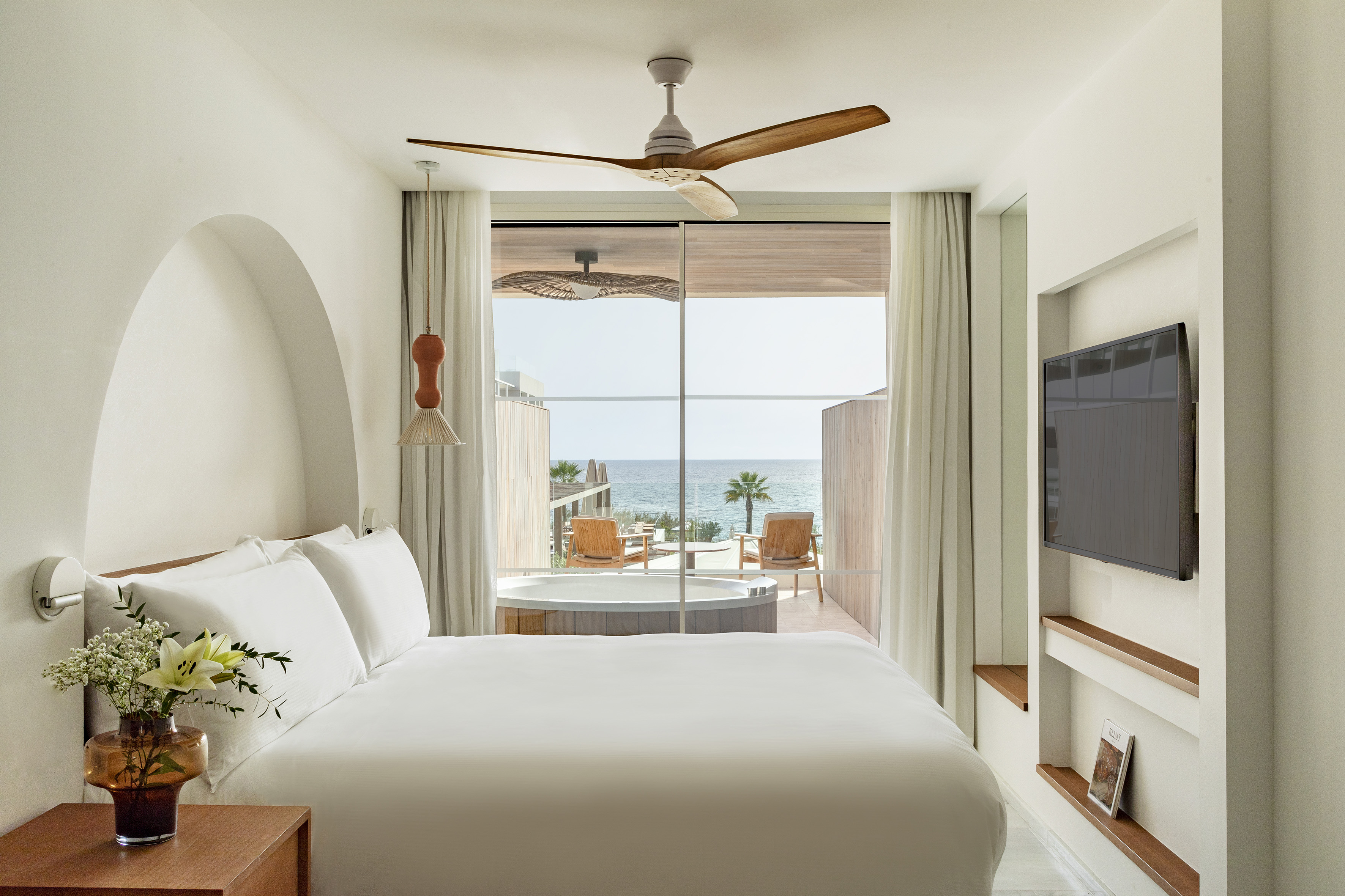Beachfront hotel room with sea view, private hot tub, and white bed.