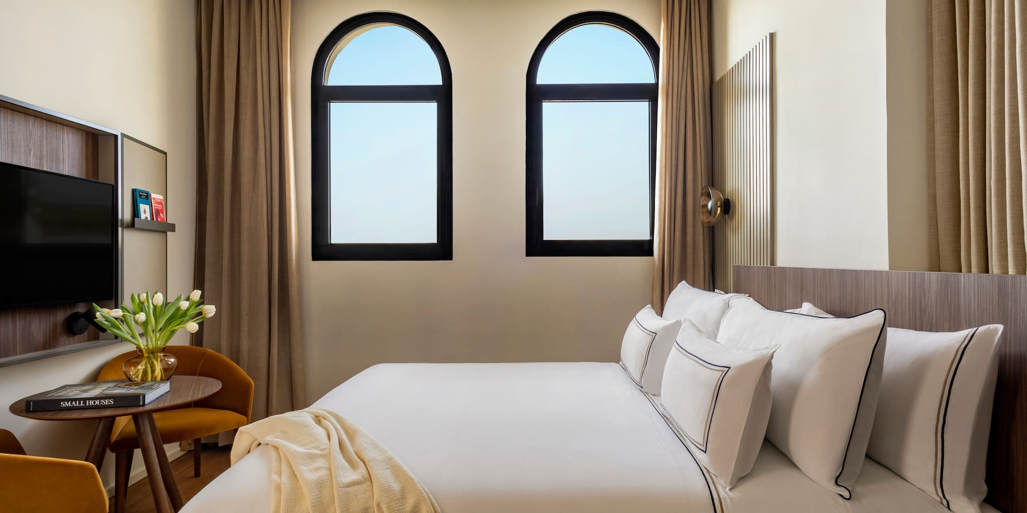 a bed with white sheets and pillows in a room with windows