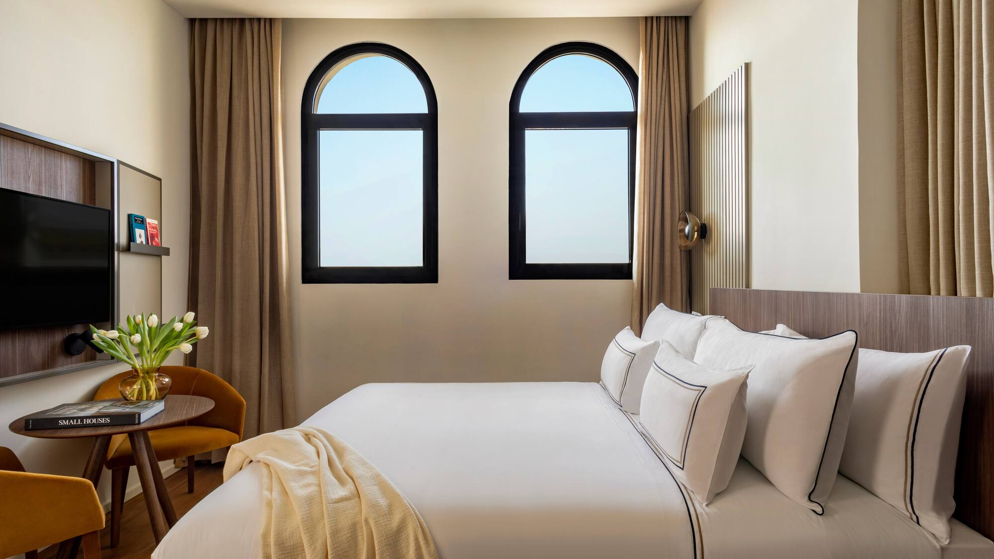 a bed with white sheets and pillows in a room with windows