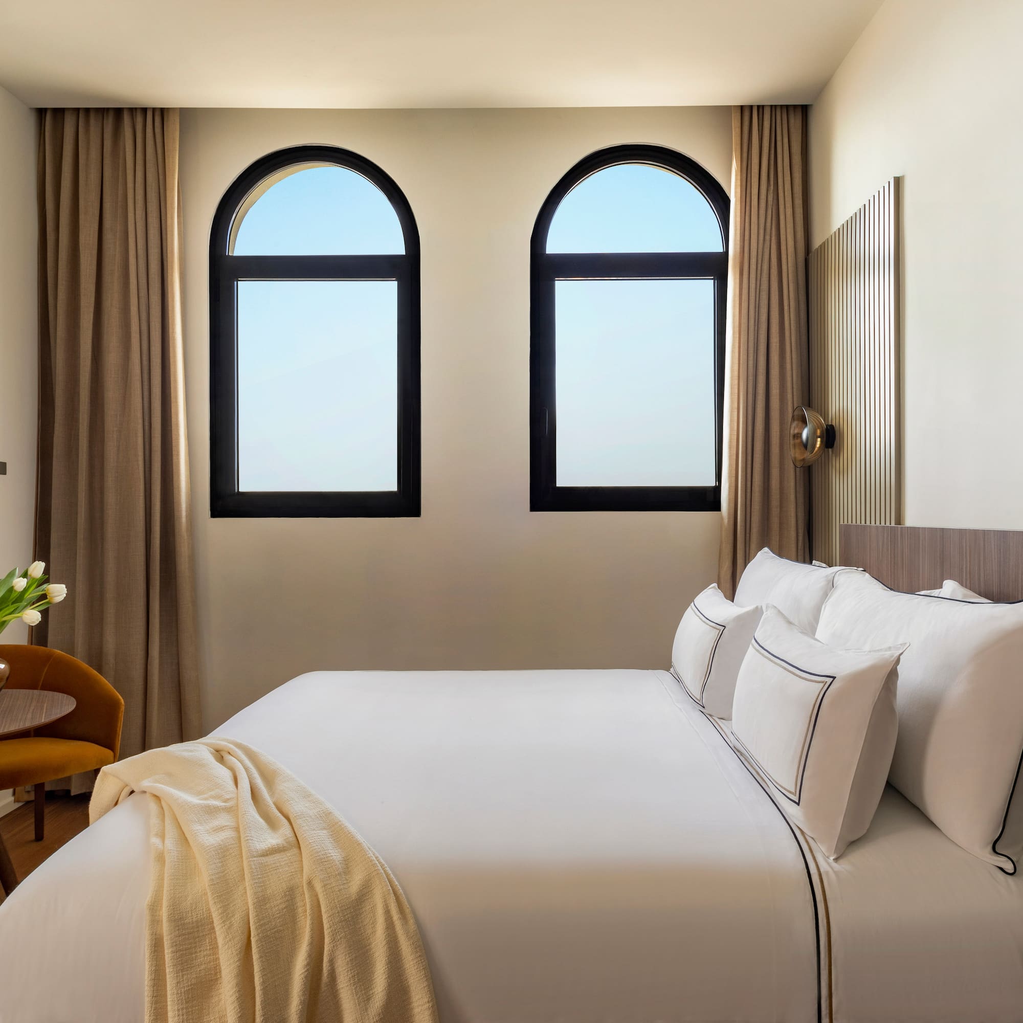 a bed with white sheets and pillows in a room with windows