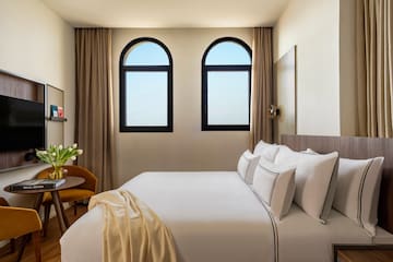 a bed with white sheets and pillows in a room with windows