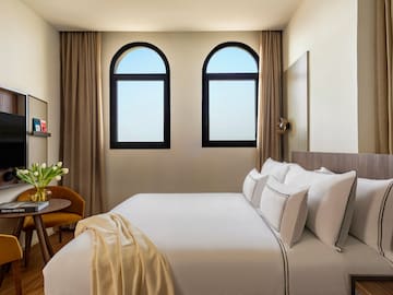 a bed with white sheets and pillows in a room with windows