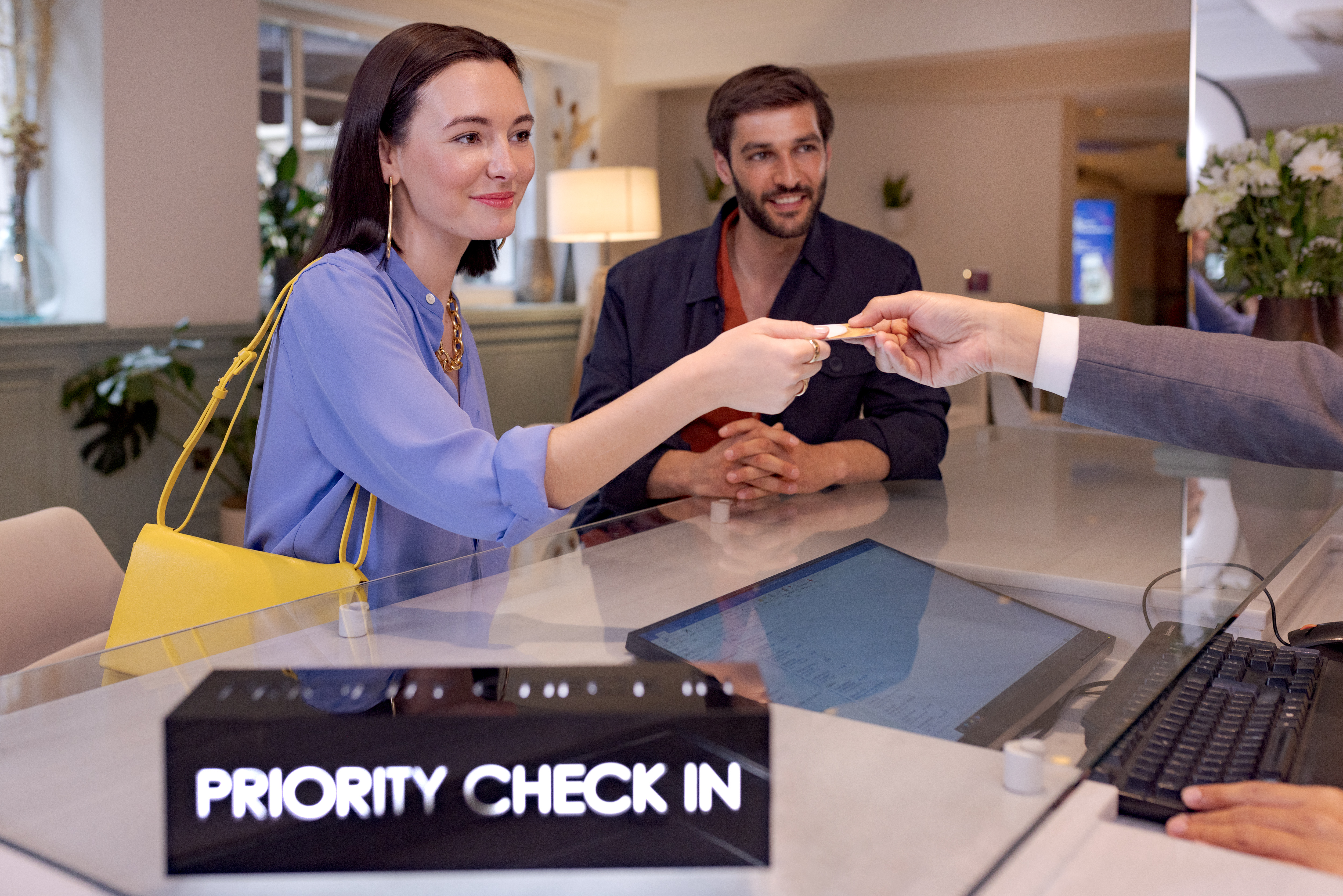 Couple at hotel priority check-in desk, receiving room key from staff.